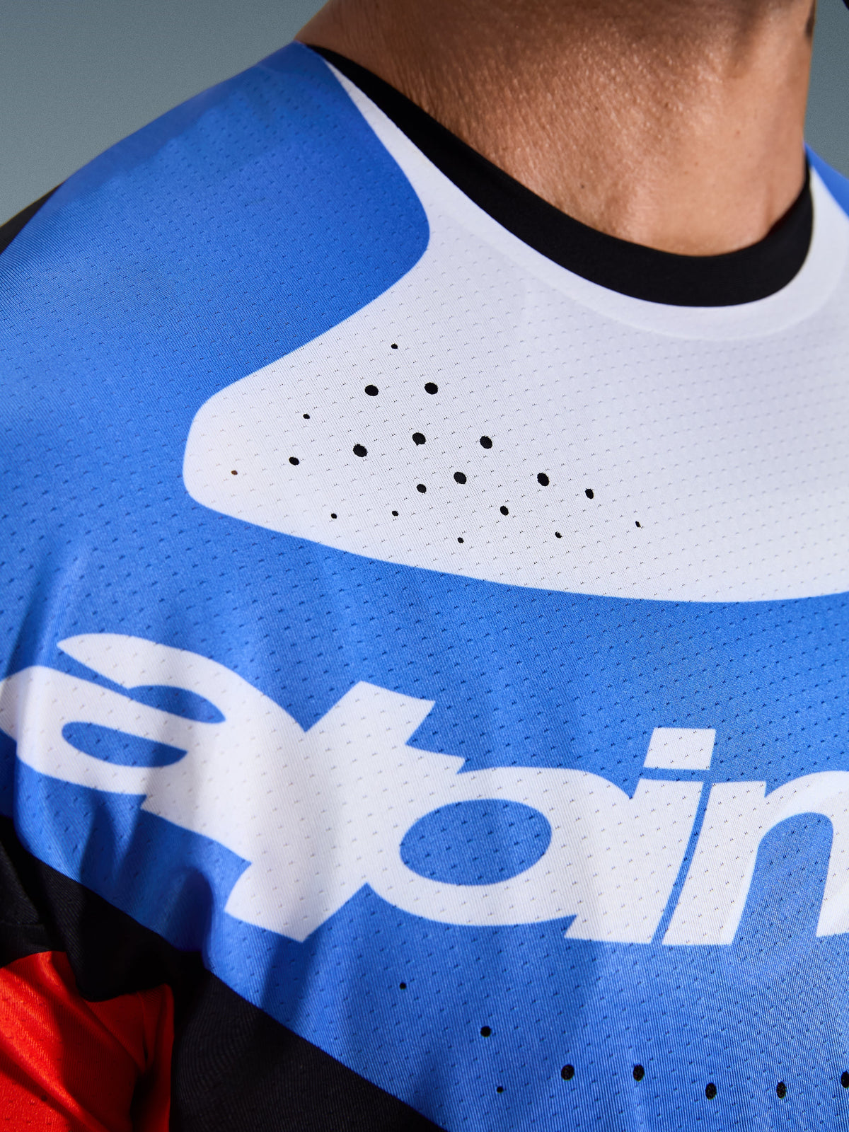 Alpinestars Techstar Knif Jersey 2026, maglia da motocross, primo piano di petto e collo, blu e bianco con colletto nero, fori di ventilazione tagliati al laser, tessuto mesh traspirante con logo Alpinestars