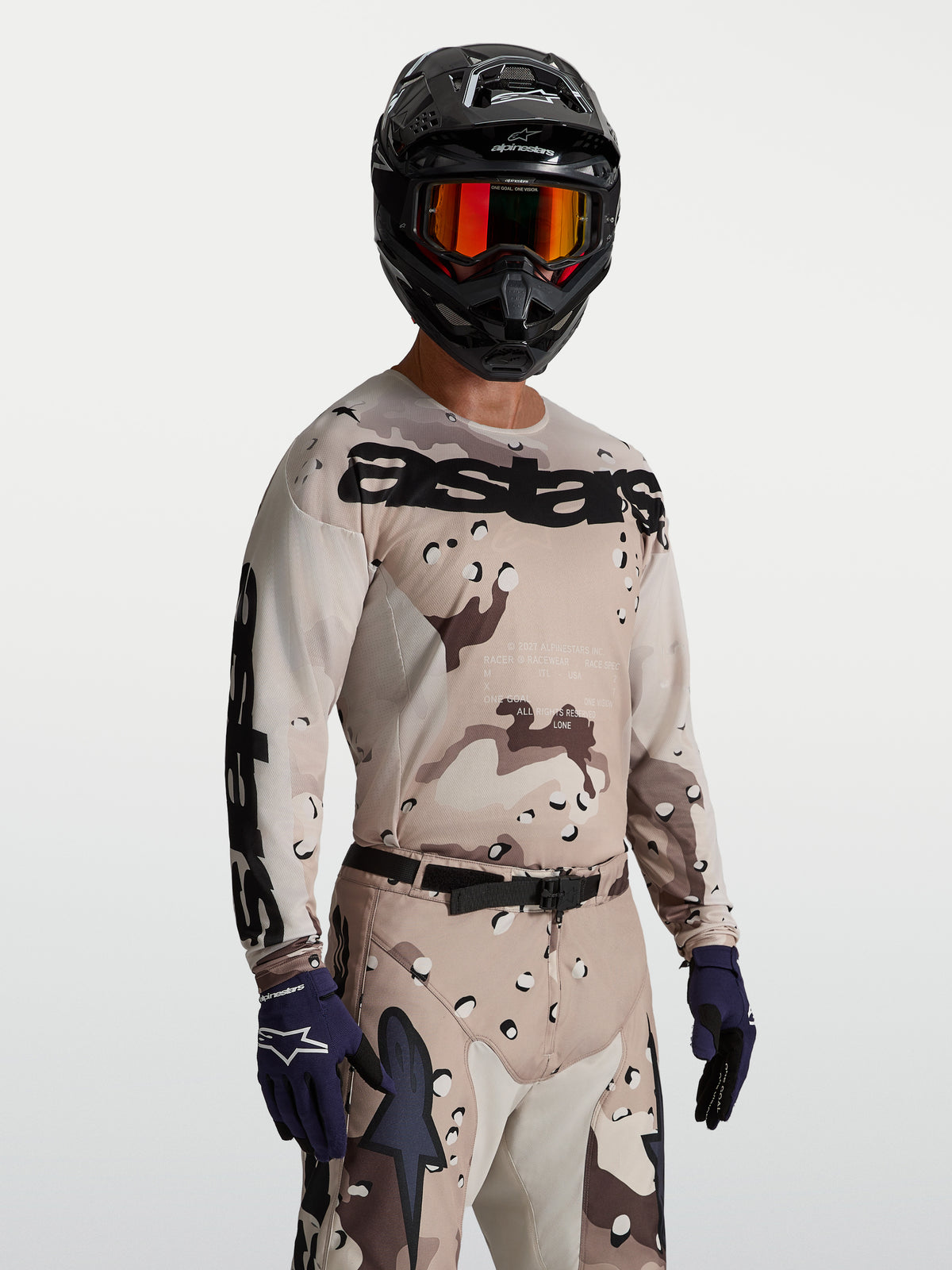 Alpinestars Maglia Racer Lone, maglia da motocross da uomo, colore sabbia desert camo e nero, tessuto tecnico traspirante, vestibilità race, indossata con casco e occhiali per sessioni off-road.