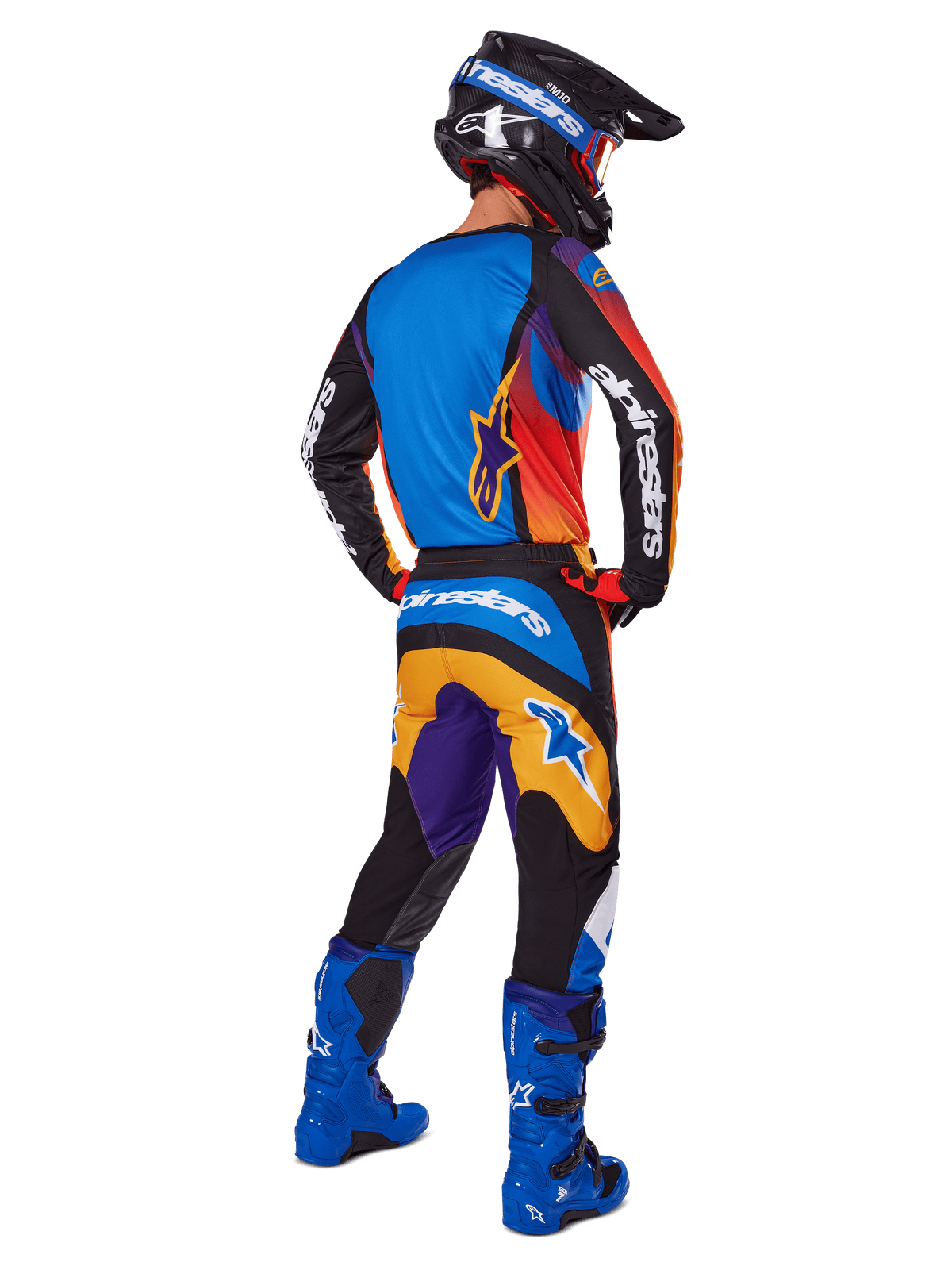 Pilota di motocross visto di spalle, set di equipaggiamento Alpinestars 2025 Fluid Wurx, maglia multicolore con pannelli blu, arancione e viola, pantaloni coordinati con logo Alpinestars bianco sulla seduta, stivali blu acceso e casco nero, outfit coordinato per gare fuoristrada