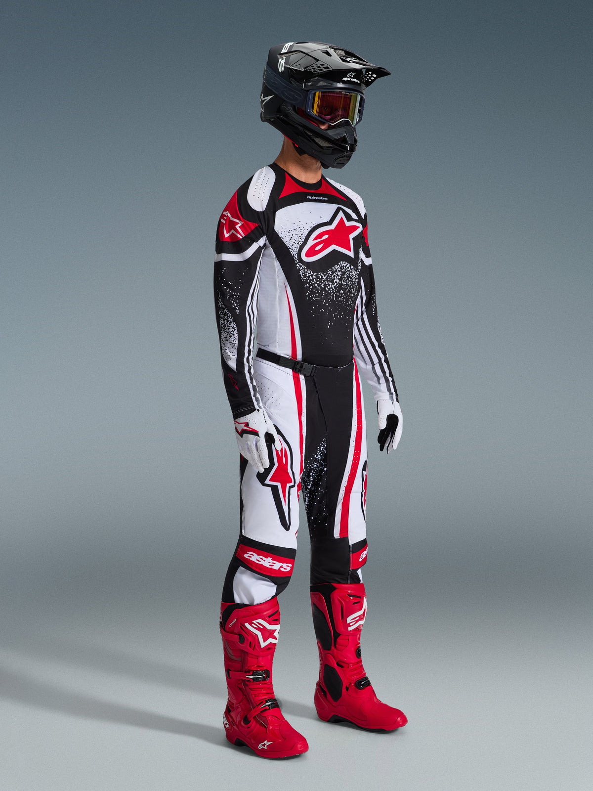 Pilota di motocross che indossa la maglia Techstar Nomur 2026, abbigliamento da gara nero, bianco e rosso, pantaloni coordinati con accenti rossi, casco nero, stivali rosso brillante, guanti bianchi e neri, outfit professionale completo da motocross per competizioni off-road.