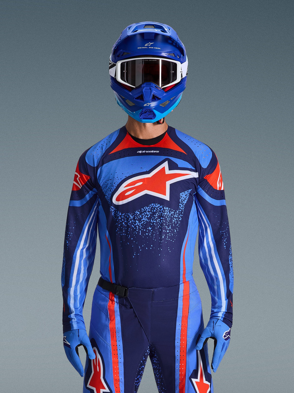 Alpinestars Maglia Techstar Nomur 2026, maglia da motocross, blu scuro, arancione e blu UCLA, indossata con pantaloni abbinati, casco blu e guanti, caratterizzata dal logo a stella bianca sul petto con linee dinamiche e motivi puntinati
