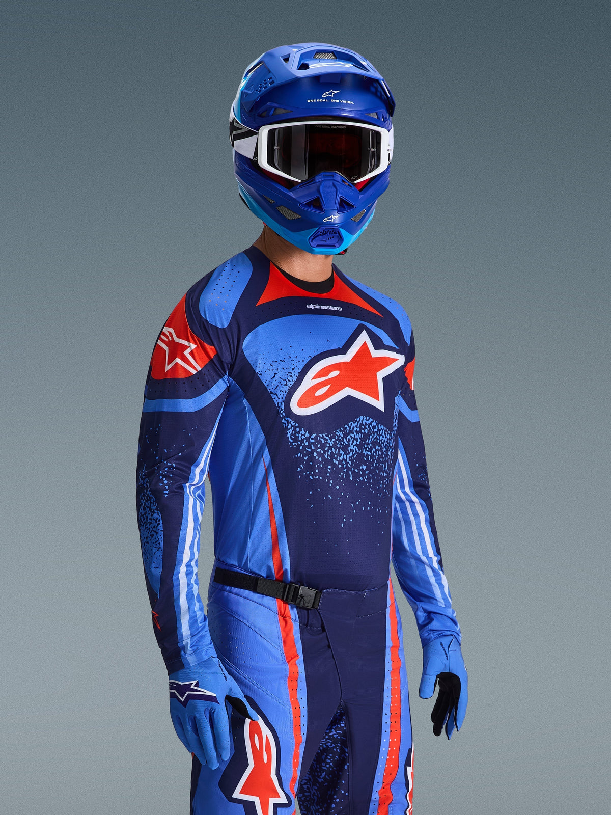 Alpinestars 2026 Techstar Nomur Gear Set, maglia e pantaloni da motocross in blu scuro, arancione e blu UCLA, indossato da un pilota con casco e guanti blu coordinati, con grafiche del logo audaci e vestibilità atletica race fit.