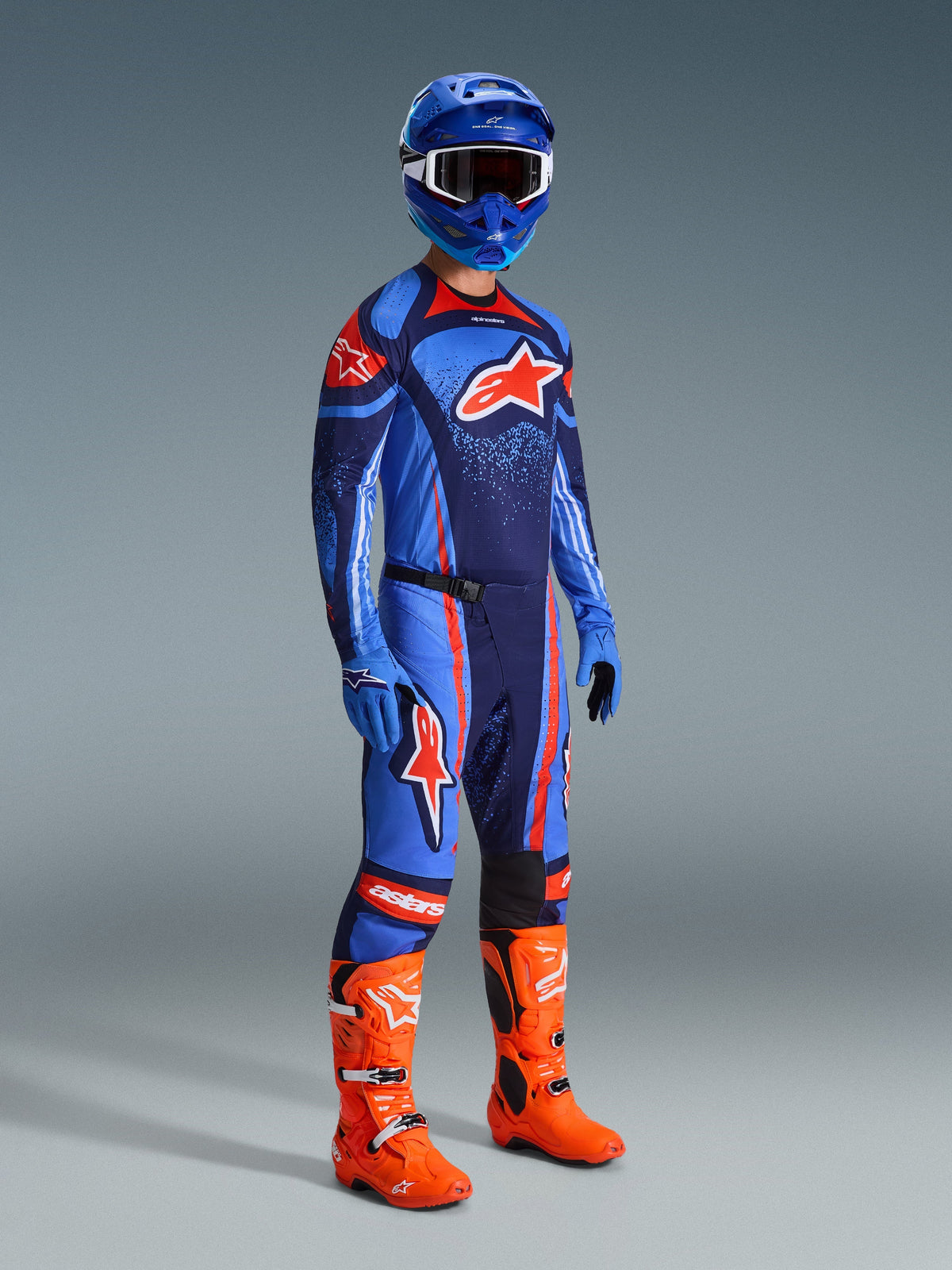 Pilota di motocross con Set Gear Alpinestars Techstar Nomur 2026, maglia blu scuro con accenti azzurri e arancioni, pantaloni coordinati con strisce arancioni, casco blu, stivali arancione acceso e guanti blu, completo da motocross per prestazioni fuoristrada