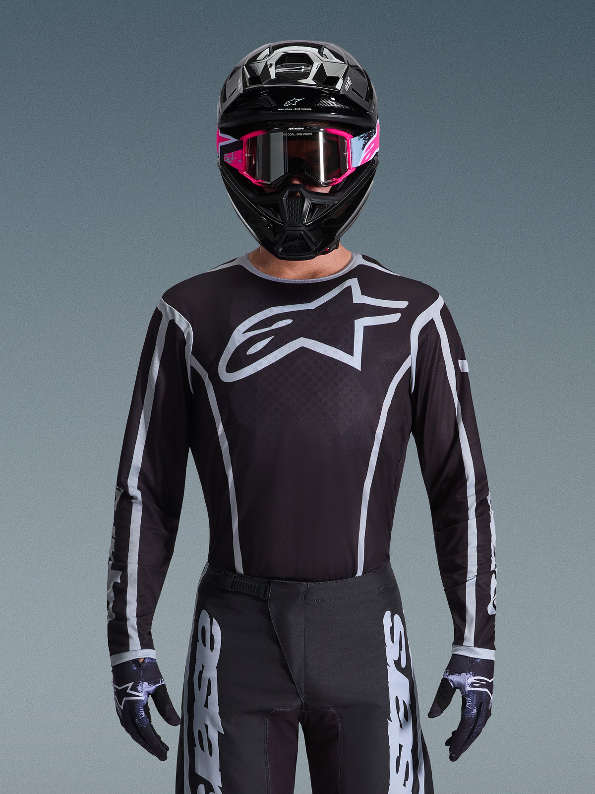Alpinestars 2026 Fluid Apex Gear Set, maglia e pantaloni da motocross in bianco e nero, caratterizzati da un grande logo sul petto e design a linee geometriche, indossato con casco nero e occhiali rosa, abbigliamento tecnico per gare di motocross fuoristrada.