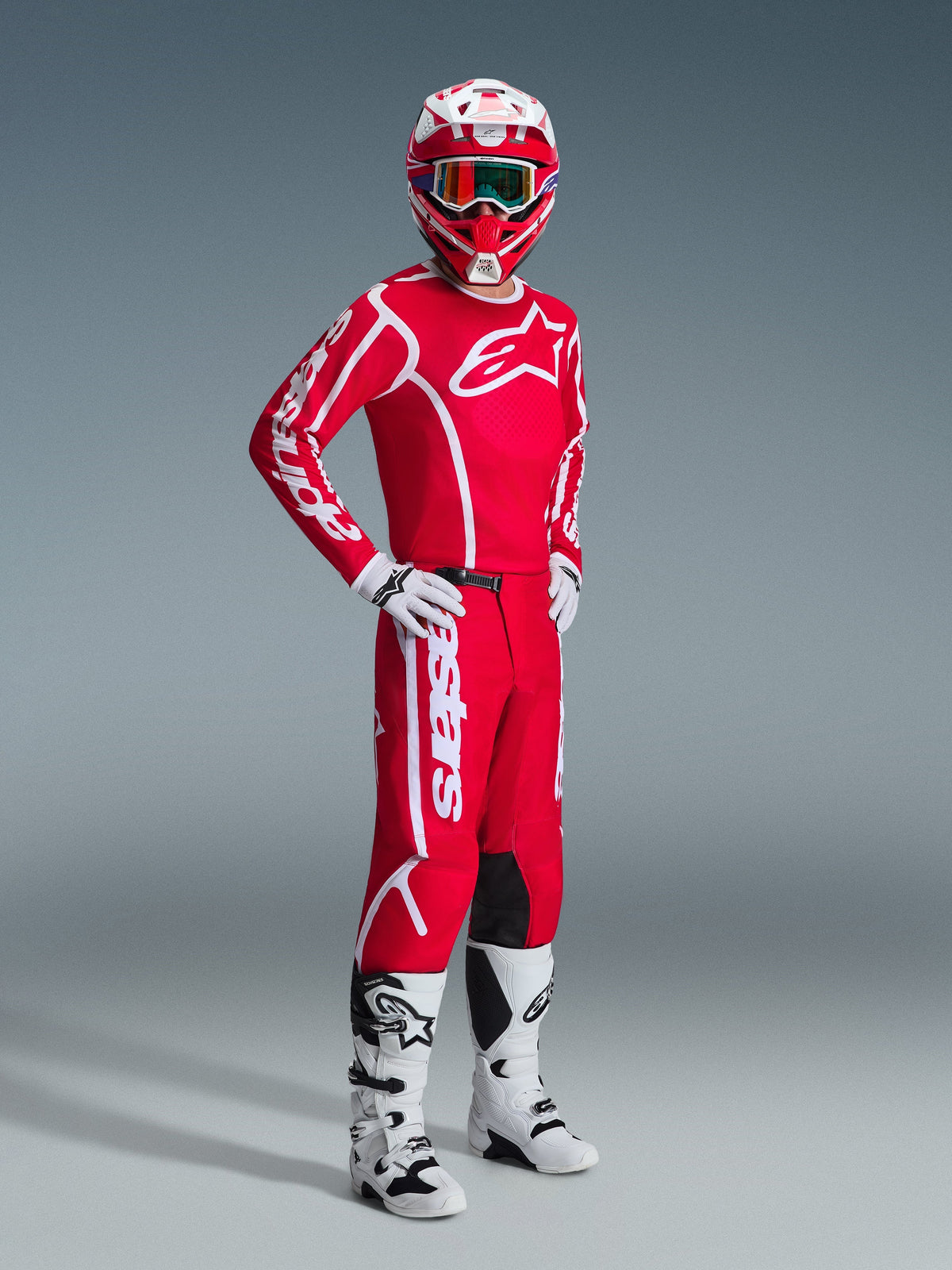 Pilota di motocross con abbigliamento completo Alpinestars, maglia 2026 Fluid Apex in rosso e bianco, pantaloni rossi coordinati con logo bianco, casco rosso e bianco con occhiali, stivali da motocross bianchi e neri e guanti bianchi, scatto in studio di attrezzatura off-road.