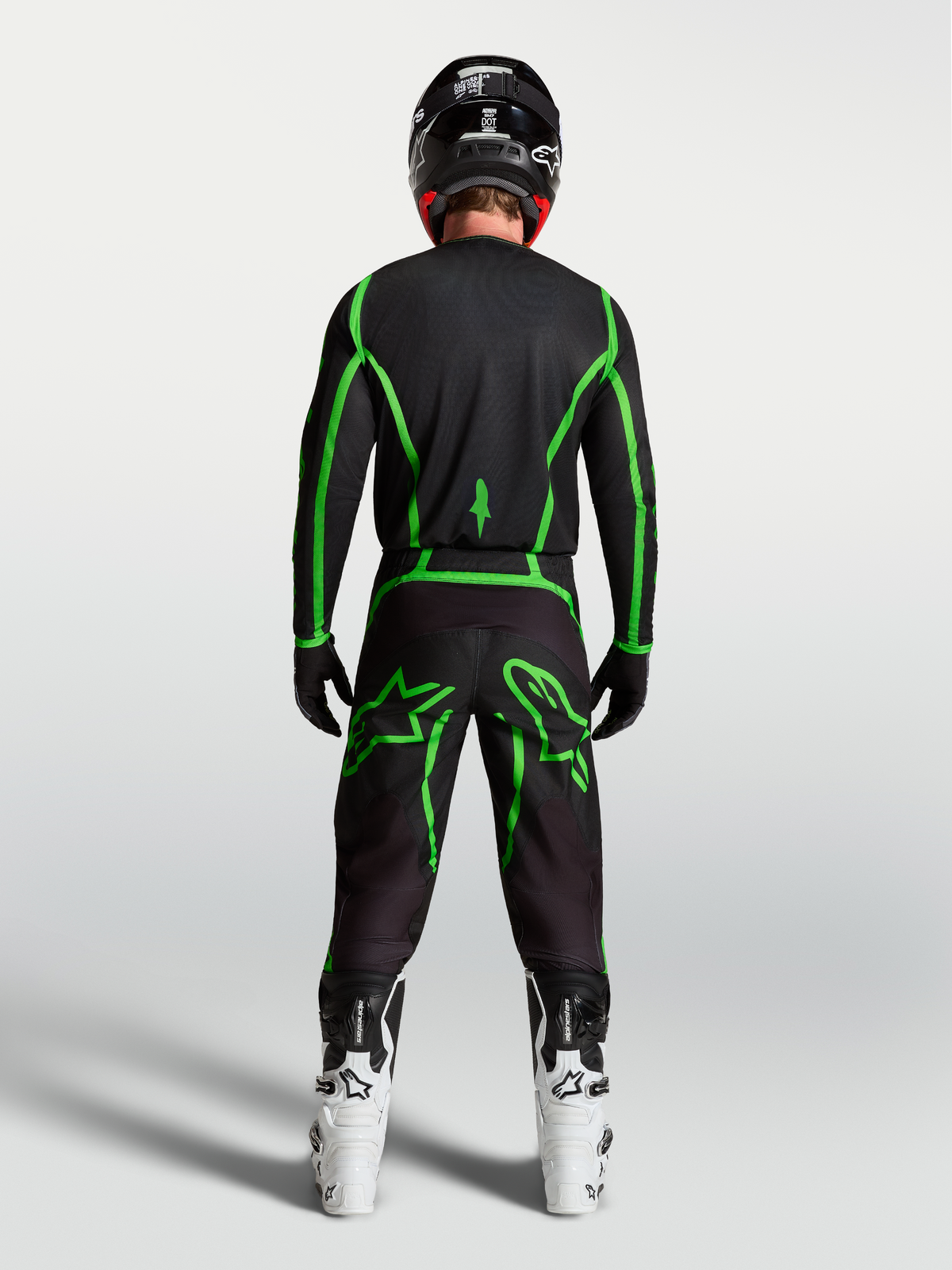 Alpinestars Pantaloni Fluid Apex V2, pantaloni da motocross da uomo, neri e verdi fluo, vista posteriore di un pilota con stivali bianchi.