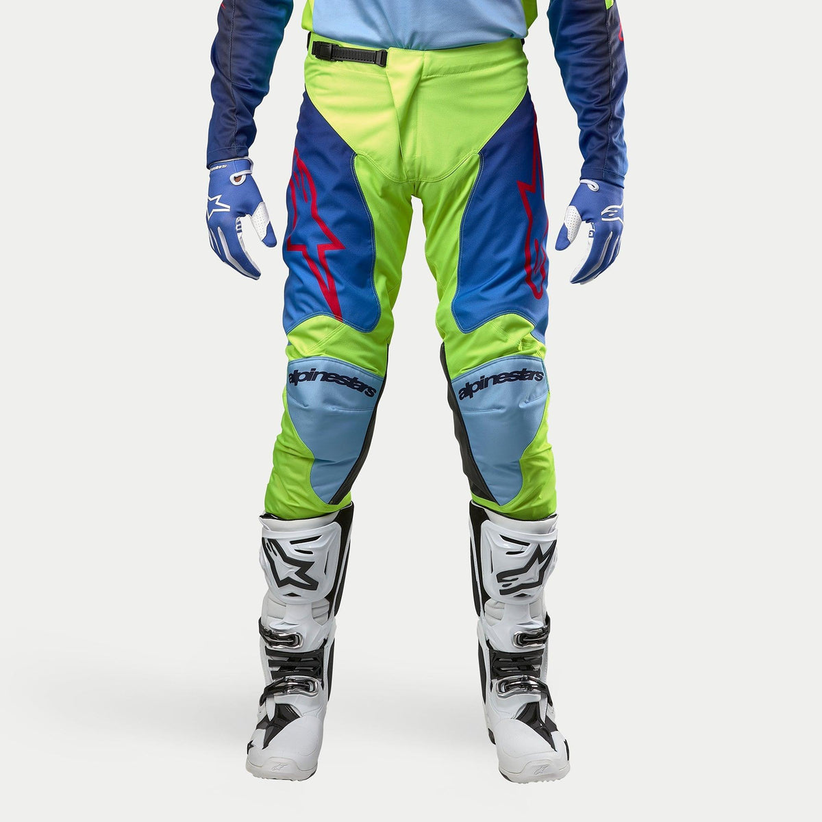 Alpinestars 2024 Racer Hoen Pants, pantaloni da motocross, Giallo Fluo e Blu Night Navy, indossati con stivali da motocross bianchi e neri e guanti blu, con loghi rossi vivaci, pannelli azzurri sulle ginocchia e un design ergonomico sportivo per la guida fuoristrada