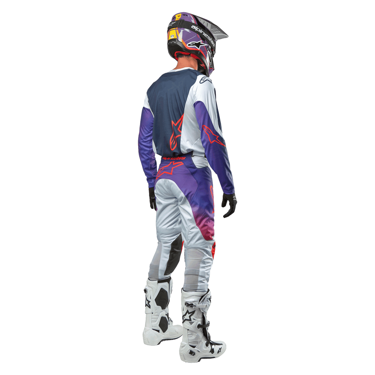Pilota di motocross visto da dietro con la maglia Alpinestars 2024 Racer Hoen in Light Gray Hot Orange Black, pannello posteriore blu navy con logo a stella arancione, maniche viola, indossata con pantaloni da gara coordinati e stivali bianchi.