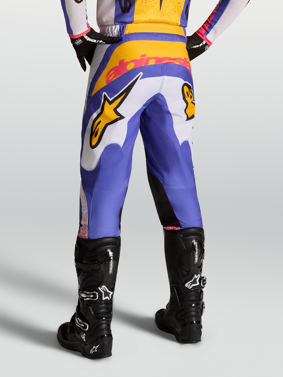 Alpinestars Pantaloni Fluid Drag, pantaloni da motocross da uomo, blu e oro, con rinforzo posteriore, indossati con stivali neri, design pre-curvato per prestazioni off-road.