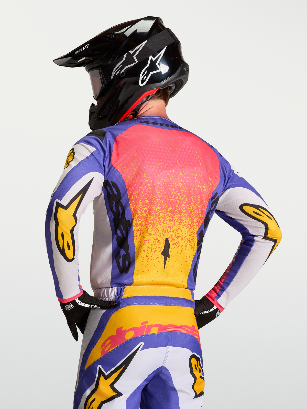 Alpinestars Maglia Fluid Drag, maglia da motocross blu iris e oro su un modello con casco, tessuto traspirante e taglio posteriore ergonomico.