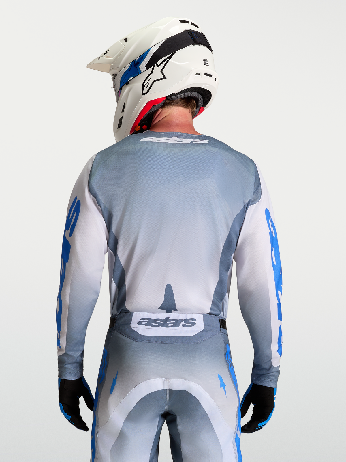 Alpinestars Maglia Racer Amber, maglia da motocross grigio e bianco, vista posteriore su modello con casco bianco, in poliestere traspirante.