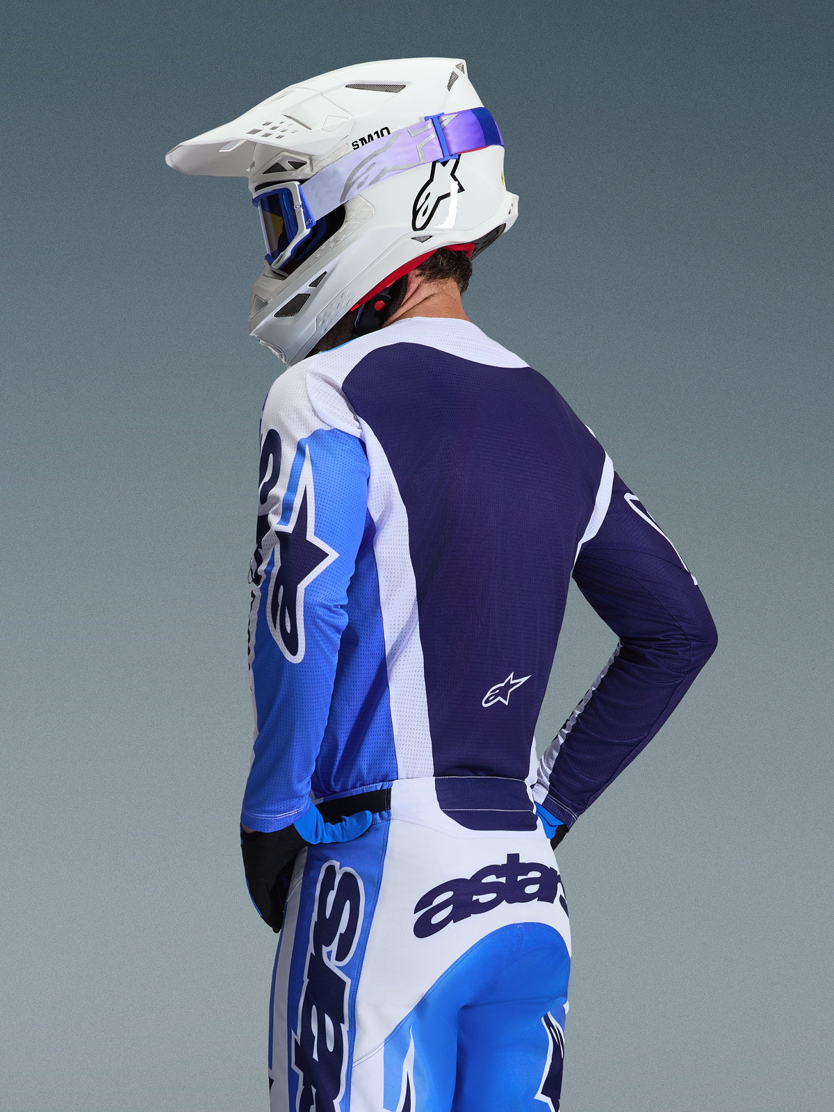 Pilota di motocross che indossa la maglia Alpinestars 2026 Racer Air Portl in blu Ucla e bianco, vista posteriore che evidenzia il pannello posteriore in mesh traspirante blu navy, abbinata a pantaloni coordinati e un casco bianco Alpinestars con occhiali blu, set di abbigliamento da motocross coordinato.