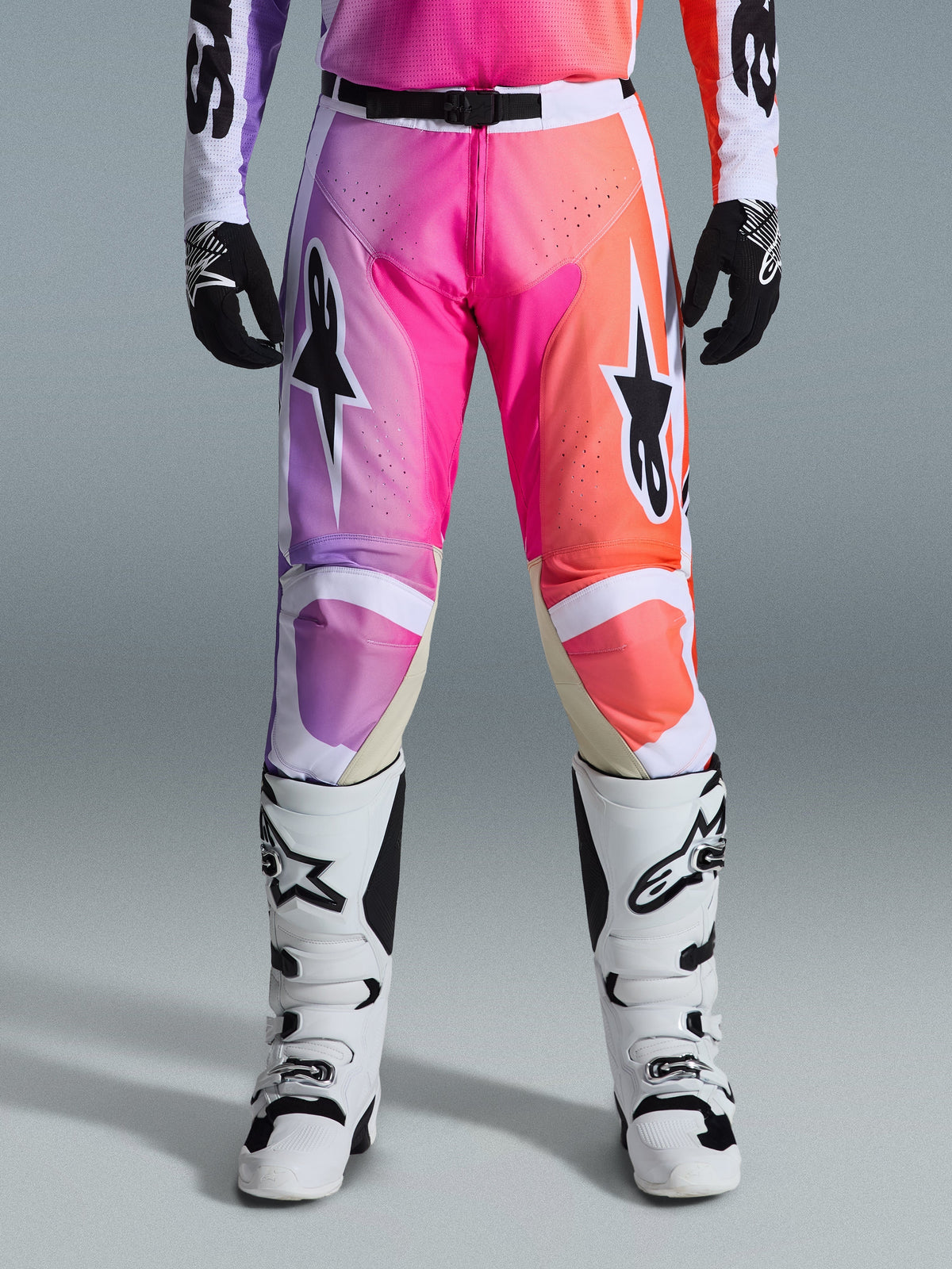 Alpinestars 2026 Racer Air Portl Pants, pantaloni da motocross, vivace sfumatura viola, rosa e arancione, con vistosi loghi a stella sulle cosce, indossati con stivali da corsa bianchi e guanti neri, progettati per la guida off-road ad alte prestazioni.