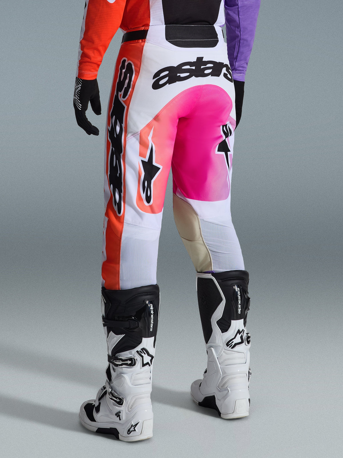 Alpinestars 2026 Racer Air Portl Pants, pantaloni da motocross, multicolore con bianco, rosa acceso e arancione, vista posteriore indossati con stivali Alpinestars bianchi e neri, con loghi evidenti e costruzione da gara resistente