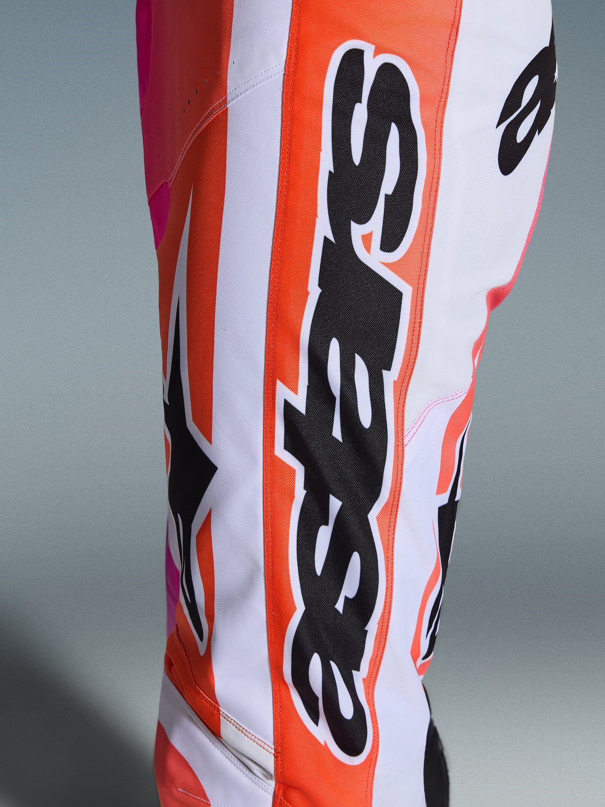 Pantaloni Alpinestars Racer Air Portl 2026, pantaloni da motocross, arancione, bianco e rosa, primo piano con grande marchio Alpinestars nero e logo a stella, tessuto traforato per la ventilazione, abbigliamento da corsa off-road resistente
