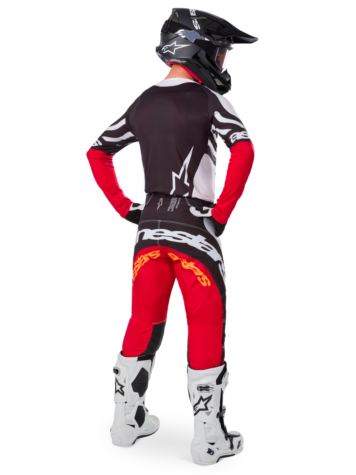 Vista posteriore di un pilota di motocross che indossa il set Limited Edition Techstar Deep Gear, con maglia nera con accenti bianchi e rossi, pantaloni rossi e neri coordinati con marchio 'Alpinestars', stivali da gara bianchi e casco nero, mostrando l'abbigliamento completo da corsa fuoristrada.