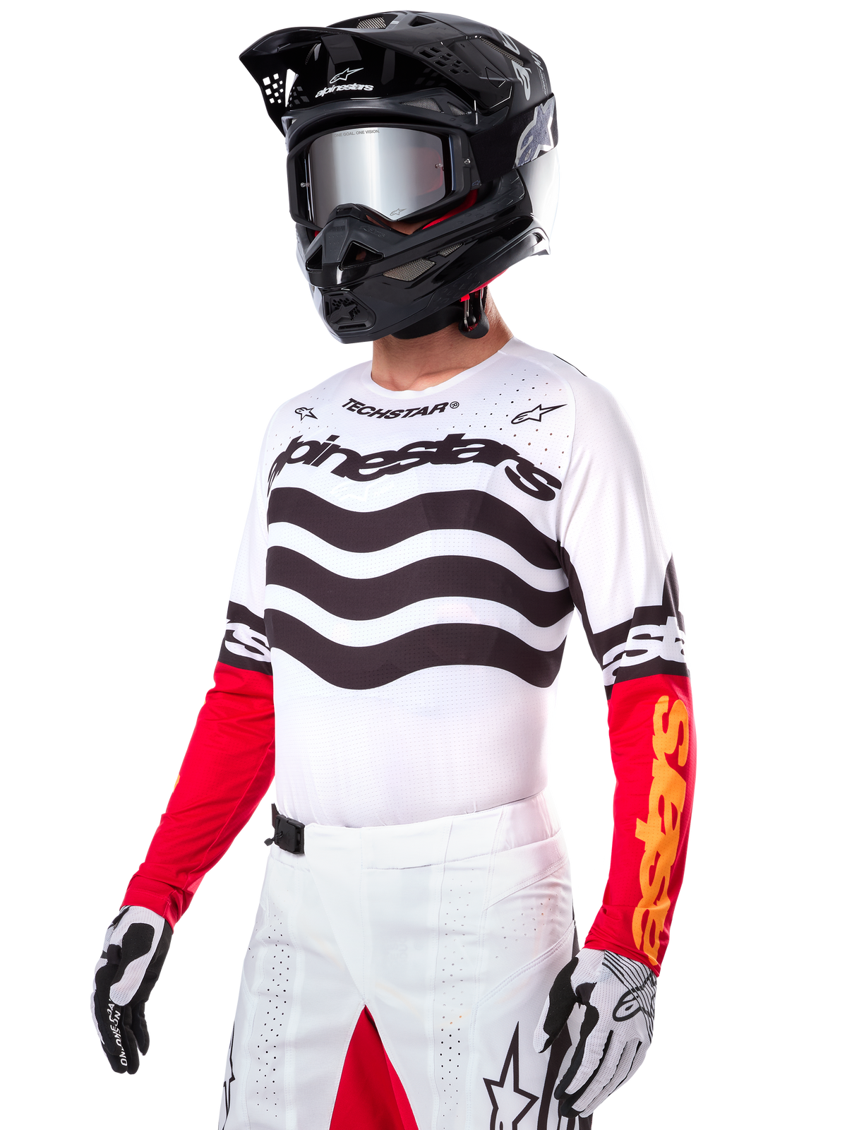 Pilota di motocross che indossa la maglia Alpinestars Limited Edition Techstar Deep, maglia bianca con strisce ondulate nere e parte inferiore delle maniche rossa, abbinata a casco nero, occhiali a specchio, guanti bianchi e neri e pantaloni da corsa bianchi, completo da motocross ad alte prestazioni.