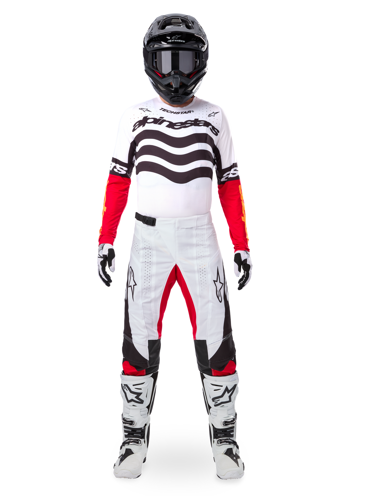 Pilota di motocross con set completo Alpinestars Limited Edition Techstar Deep, maglia bianca con grafiche a onde nere e maniche rosse, pantaloni coordinati bianchi e neri con accenti rossi, casco nero con occhiali scuri e stivali bianchi, abbigliamento professionale da gara fuoristrada
