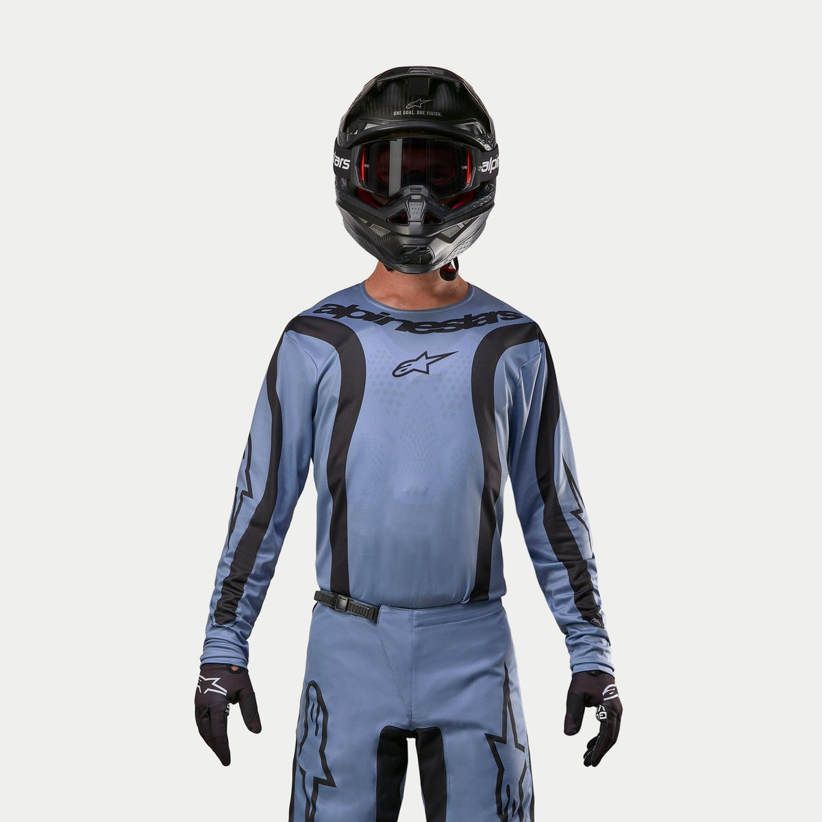 Alpinestars 2024 Fluid Lurv Jersey, maglia da motocross, azzurro e nero, indossata da un pilota con pantaloni coordinati, casco nero con occhiali rossi e guanti neri, completo coordinato per corse fuoristrada