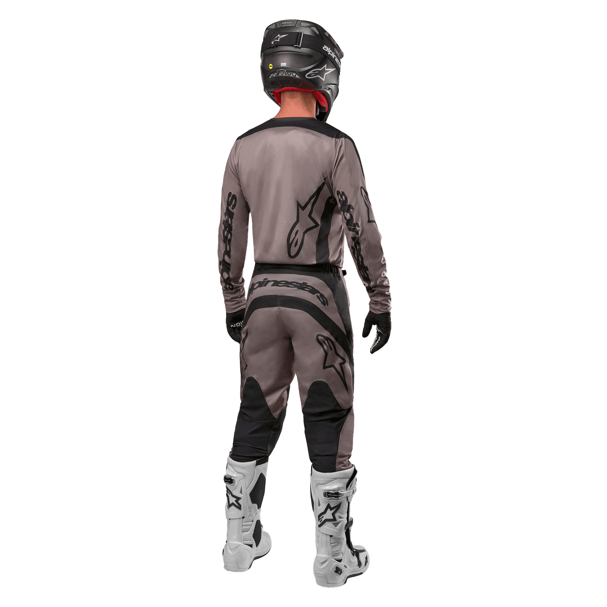 Alpinestars 2024 Fluid Lurv Jersey, maglia da motocross, Mud Black, vista posteriore di un pilota di motocross che indossa un completo da gara coordinato, casco nero e stivali bianchi, con grandi loghi Alpinestars neri e vestibilità atletica per prestazioni off-road.