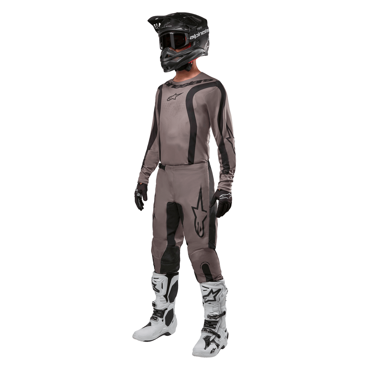 Pilota di motocross con abbigliamento da gara completo, maglia Alpinestars Fluid Lurv 2024 in Mud Black, pantaloni coordinati, casco nero con occhiali, stivali bianchi e neri e guanti neri, completo coordinato per corse off-road