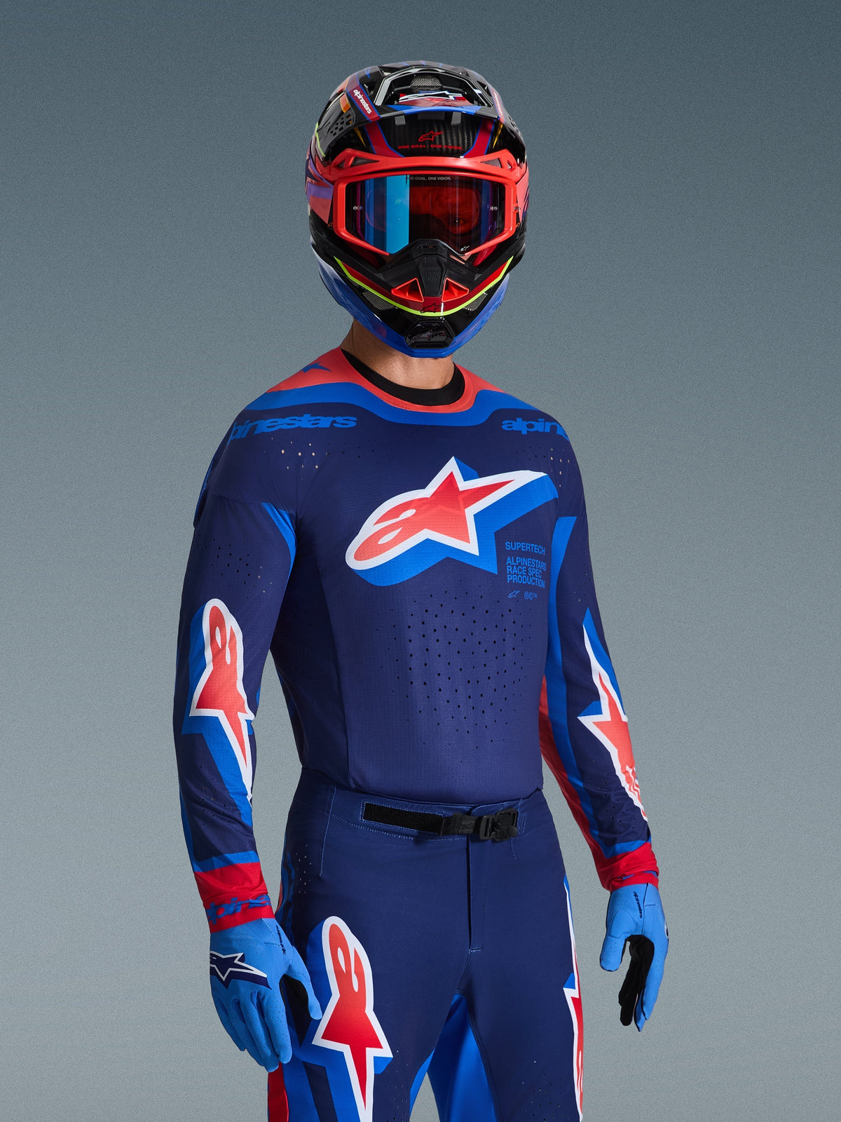 Pilota di motocross con Maglia Supertech Vista 2026 in Dark Navy, Hot Coral e Cobalt, pantaloni e guanti coordinati, casco multicolore con maschera rossa, set di abbigliamento professionale per gare fuoristrada