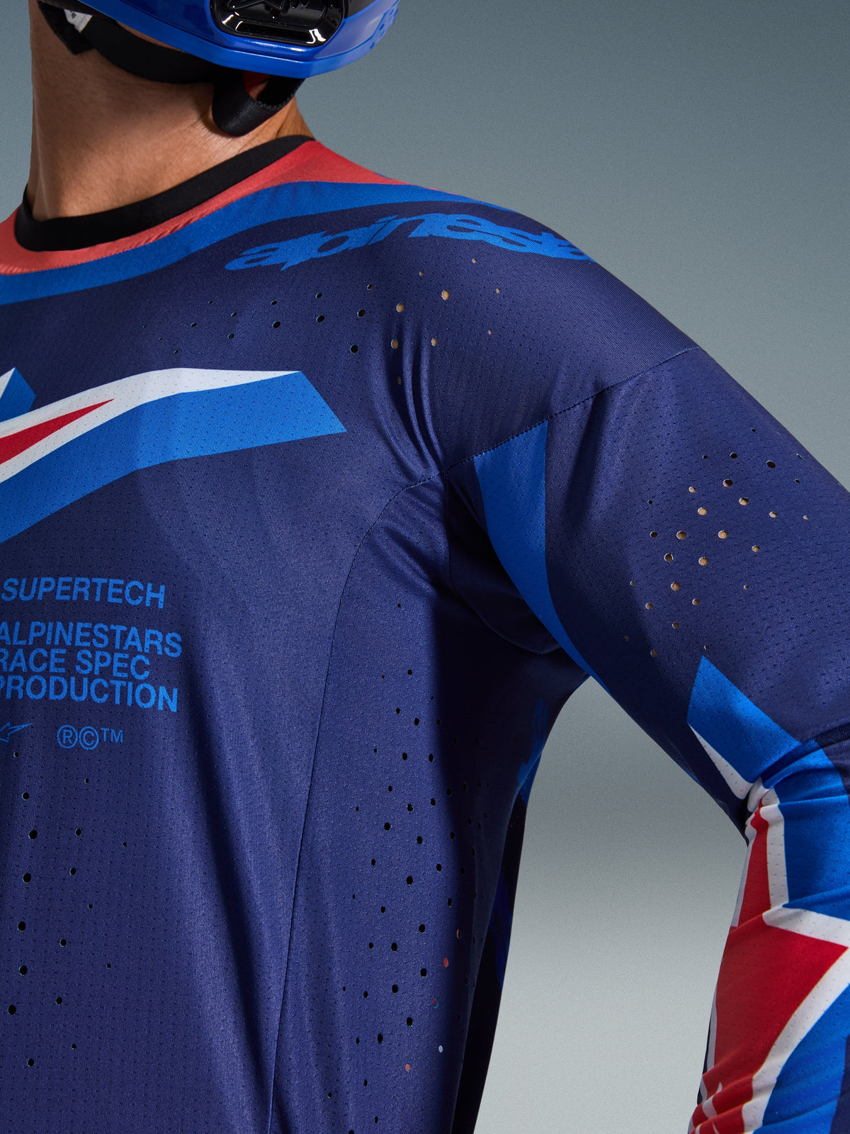 Maglia Alpinestars Supertech Vista 2026, maglia da motocross, blu scuro con accenti Hot Coral e Cobalt, primo piano che mostra le perforazioni di ventilazione tagliate al laser e la trama in mesh traspirante, marchio 'Supertech Race Spec', abbigliamento da gara professionale