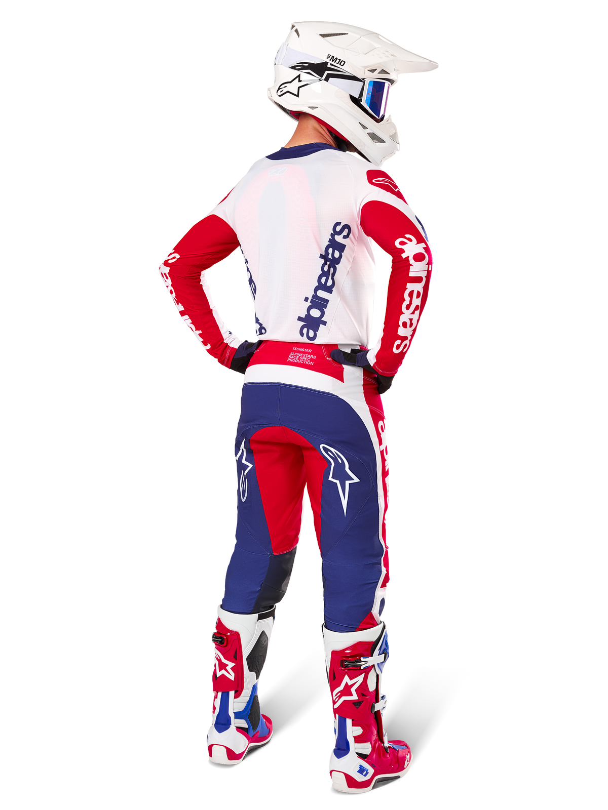 Pilota di motocross visto di spalle con maglia e set Alpinestars Limited Edition Techstar Fortitude, colorazione rosso, bianco e blu, branding Alpinestars bianco su maniche rosse e logo navy sulla schiena bianca, casco da motocross bianco e stivali coordinati.