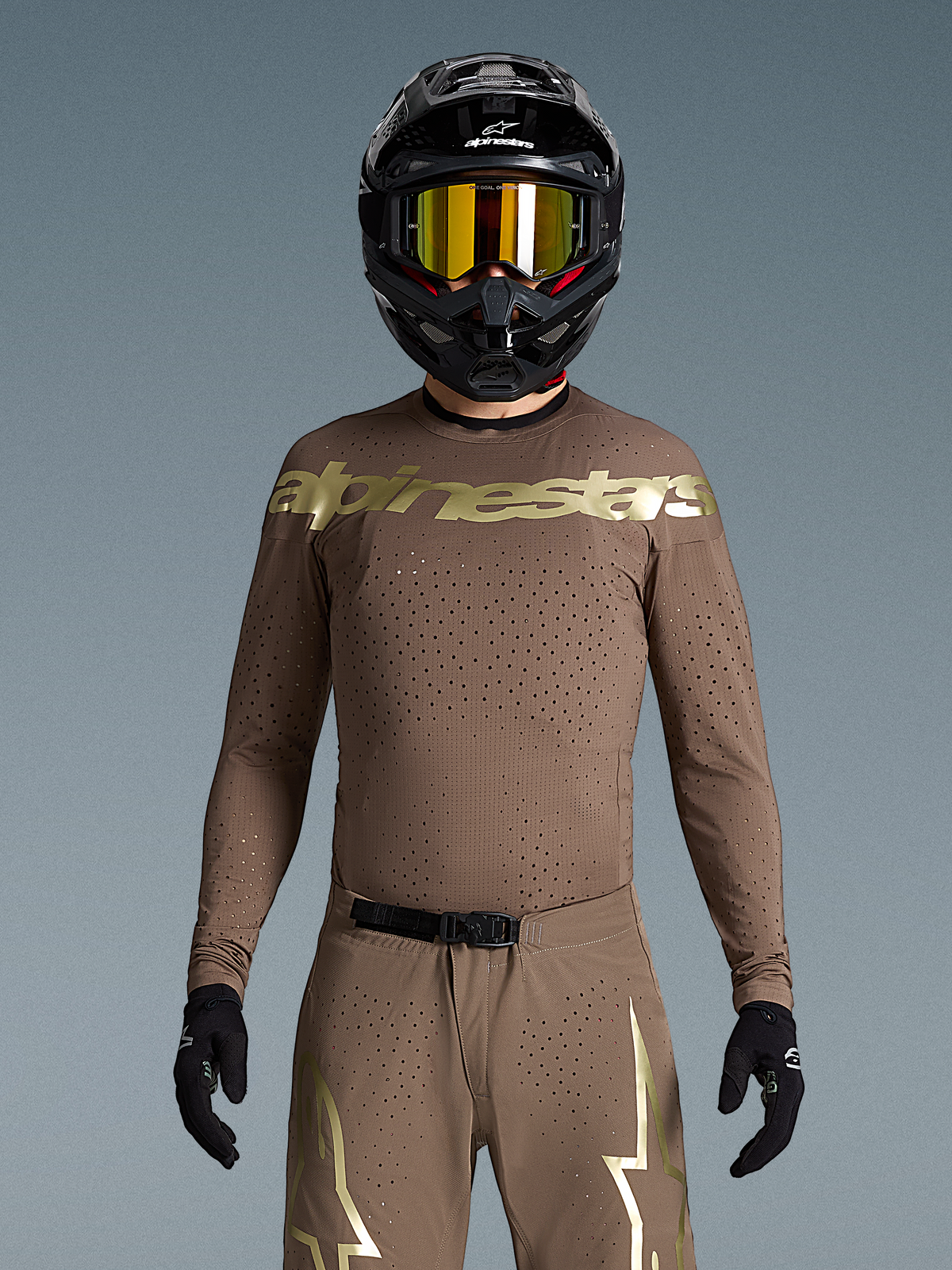 Alpinestars completo Supertech Air Gold, kit motocross uomo marrone e oro, maglia traforata al laser, indossato con casco nero.