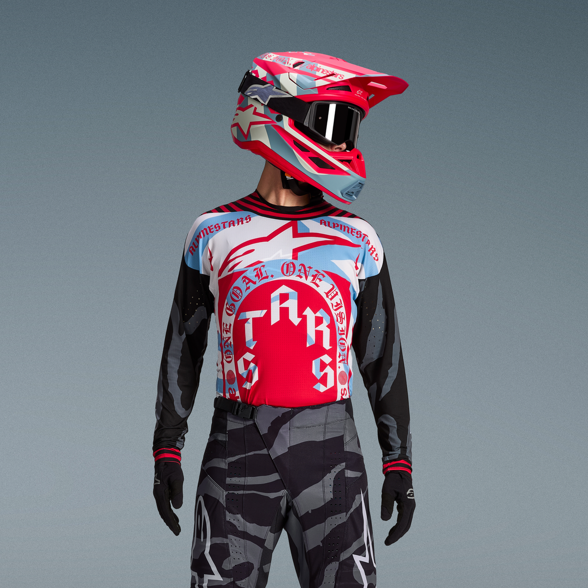 Completo Techstar Beast Coast, maglia grafica rossa e blu, pantaloni camouflage e casco rosa vivace.