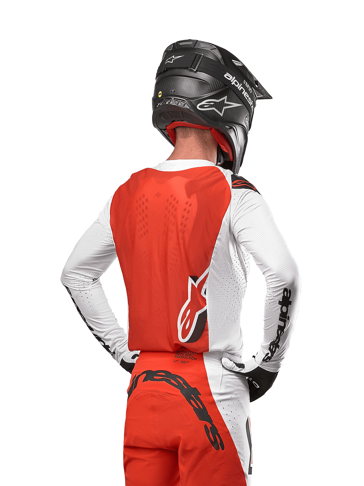 Pilota di motocross con maglia Alpinestars Supertech Ward 2024 in White Hot Orange, vista posteriore con pannello posteriore arancione e maniche bianche con branding Alpinestars nero, abbinata a pantaloni coordinati e casco nero, attrezzatura professionale per corse fuoristrada