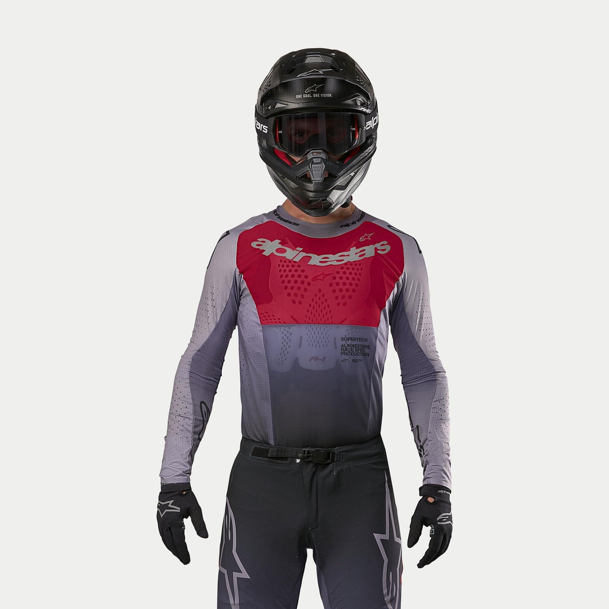 Pilota di motocross che indossa la maglia Alpinestars Supertech Dade 2024 in Iron Red Berry, caratterizzata da un pannello rosso sul petto e maniche grigie con branding argento, abbinata a pantaloni coordinati, casco nero e guanti neri, equipaggiamento professionale da gara fuoristrada
