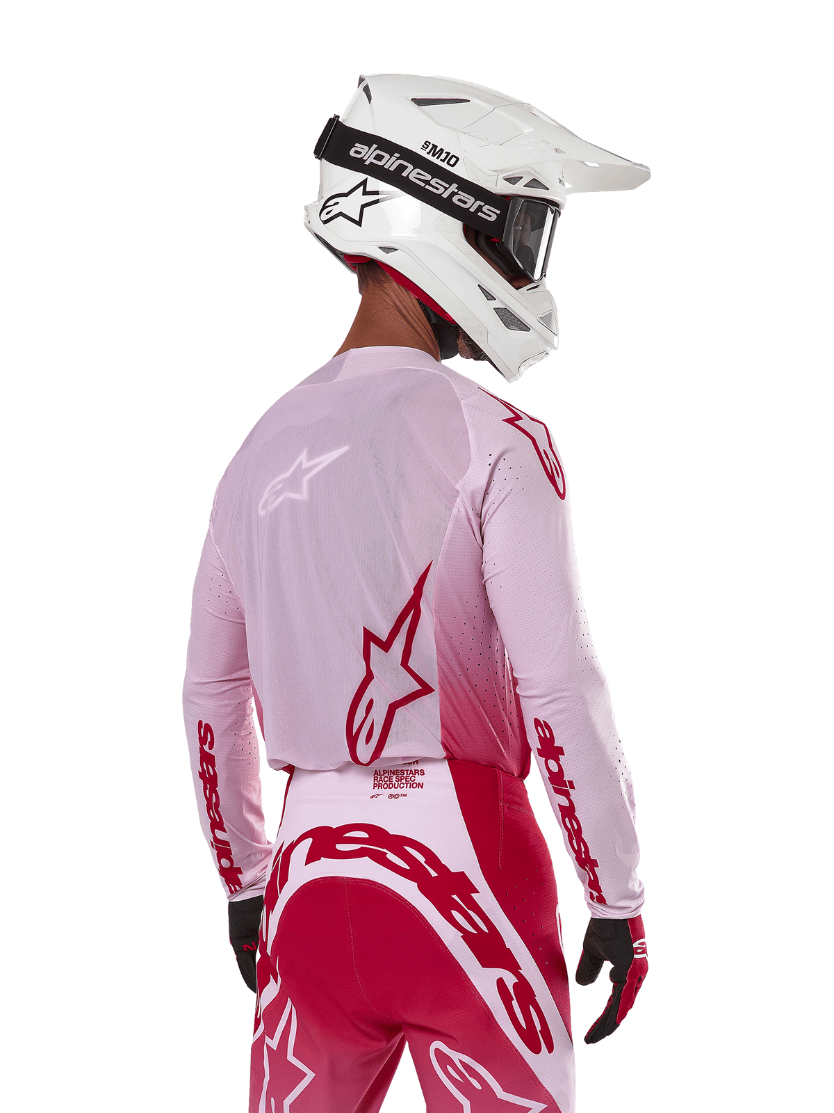 Pilota di motocross visto di spalle che indossa la maglia Alpinestars Supertech Dade 2024 in Red Berry Lilac, con pannelli in rete traspirante e loghi Alpinestars rossi, abbinata a pantaloni coordinati rossi e lilla e un casco Alpinestars bianco con maschera, abbigliamento professionale da gara off-road