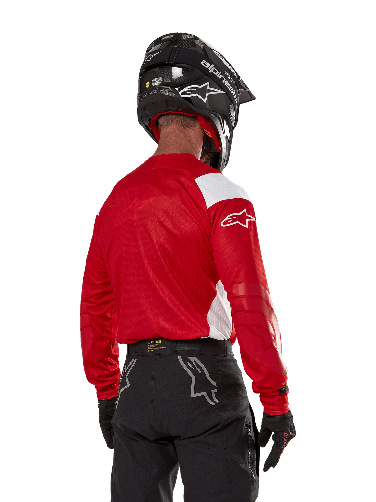 Pilota di motocross visto dal retro che indossa la maglia Alpinestars Techdura in rosso vivo con pannelli bianchi, abbinata a pantaloni da fuoristrada neri, casco nero e guanti neri, abbigliamento coordinato per la guida enduro e motocross.