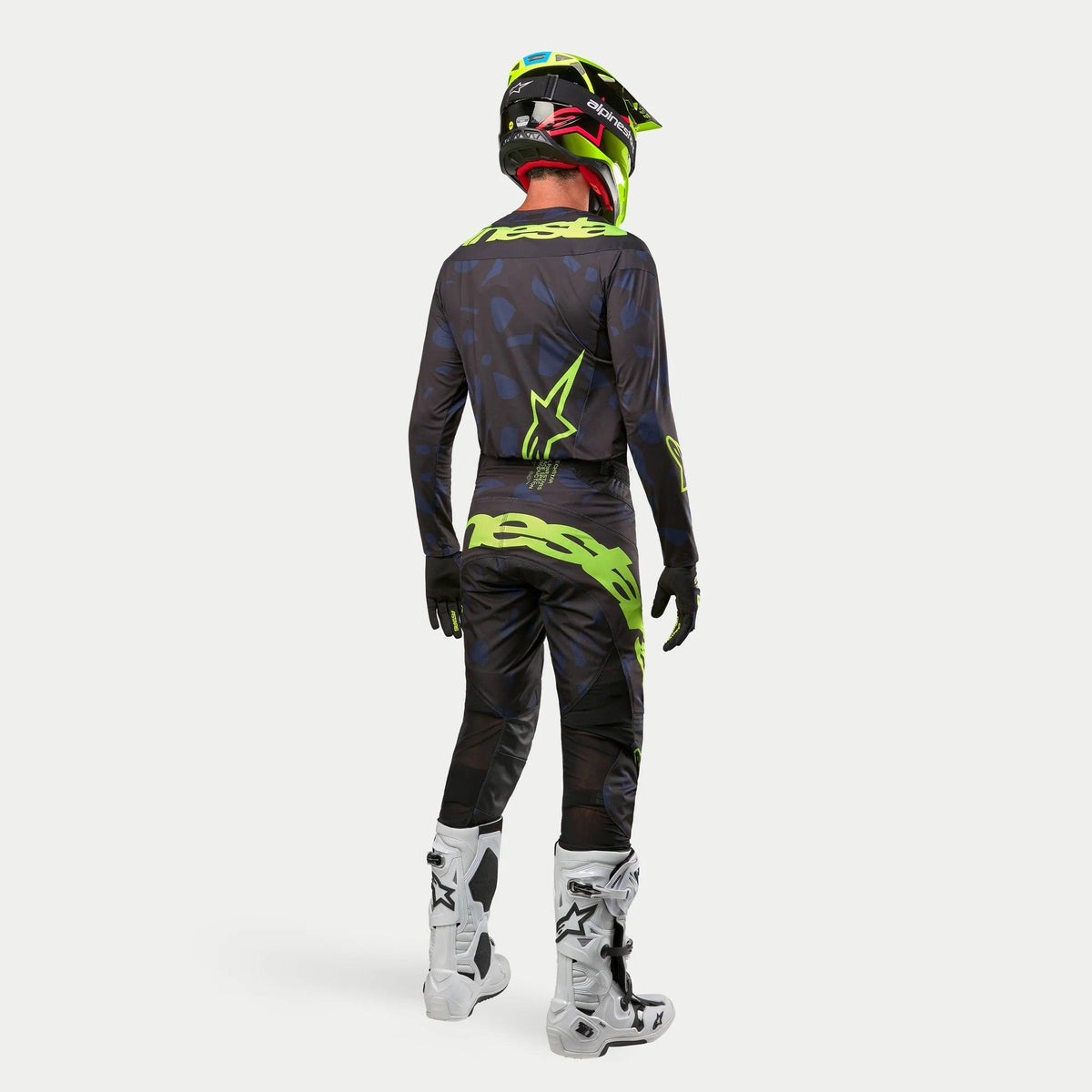 Maglia Alpinestars Techstar Rantera 2024, maglia da motocross, nero, navy e giallo fluo, indossata con pantaloni coordinati, stivali bianchi e neri e casco giallo fluo, vista dal retro in abbigliamento completo da fuoristrada