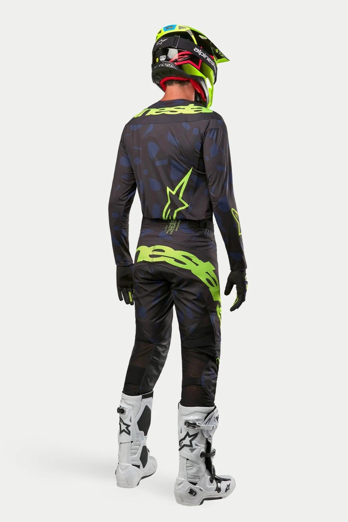 Maglia e pantaloni Alpinestars Techstar Rantera 2024, pilota di motocross con abbigliamento completo visto da dietro, nero, blu navy e giallo fluo, casco giallo fluo coordinato e stivali bianchi, completo da gara fuoristrada coordinato