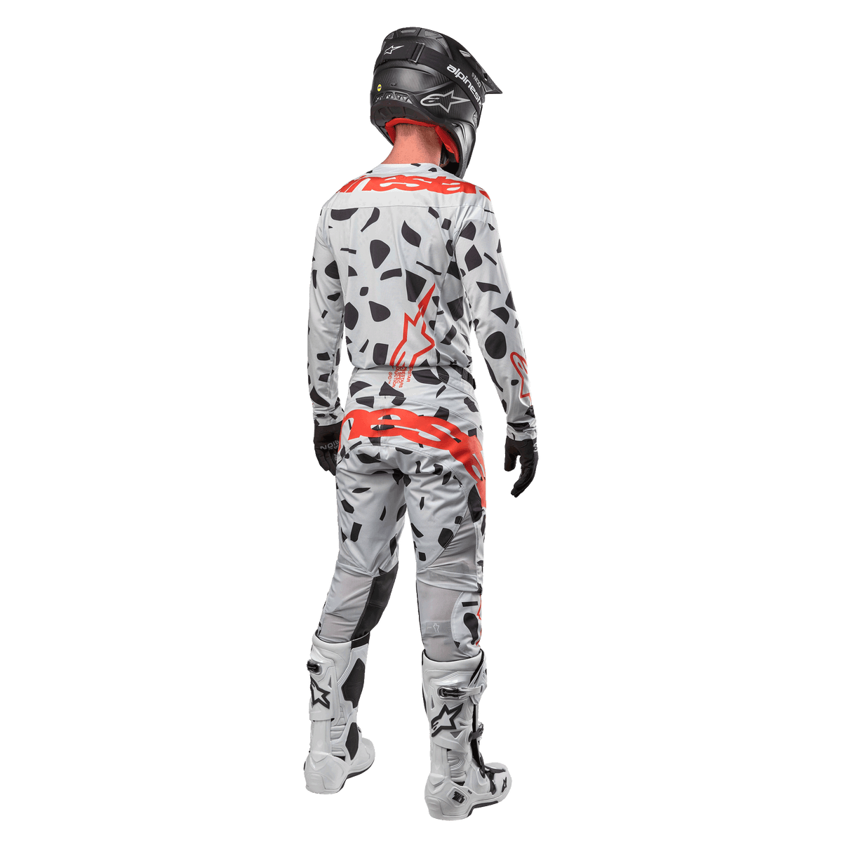 Pilota di motocross visto da dietro con maglia Alpinestars 2024 Techstar Rantera e pantaloni coordinati, motivo Haze Gray Camo con vivaci loghi Alpinestars rossi, casco nero, stivali bianchi e neri, guanti neri, set completo di abbigliamento da motocross coordinato.