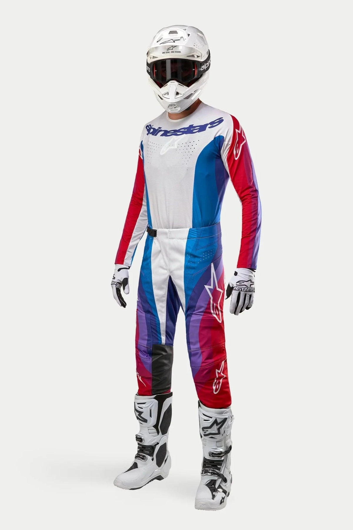 Pilota di motocross con abbigliamento completo Alpinestars, pantaloni Techstar Pneuma 2024 in Blue Mars Red White, maglia a maniche lunghe coordinata, casco bianco con occhiali scuri e stivali bianchi e neri, completo per gare fuoristrada.