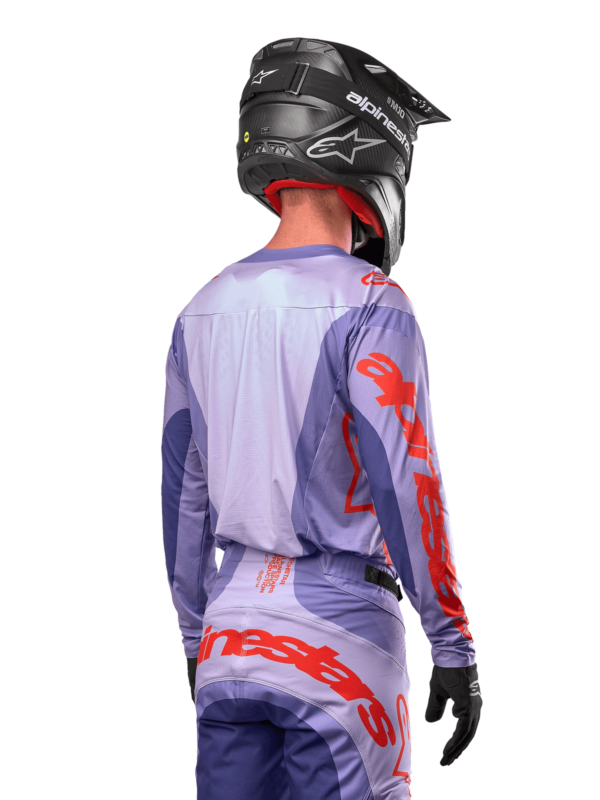 Alpinestars Techstar Ocuri Jersey 2024, maglia da motocross, viola e arancione acceso, vista posteriore su un pilota con equipaggiamento coordinato e casco nero, con grandi scritte Alpinestars arancioni sulle maniche e sulla parte bassa della schiena