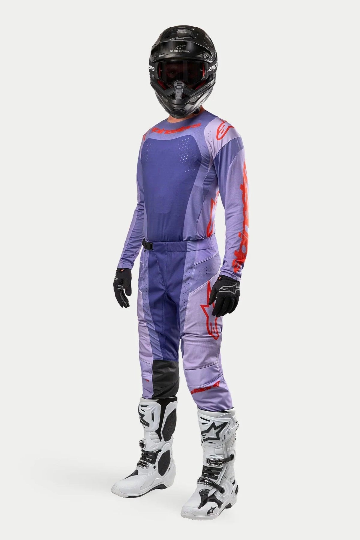Pilota di motocross che indossa la maglia Alpinestars 2024 Techstar Ocuri in viola e arancione acceso, pantaloni da gara viola coordinati con accenti arancioni, casco nero, stivali bianchi e neri e guanti neri, equipaggiamento completo da competizione fuoristrada