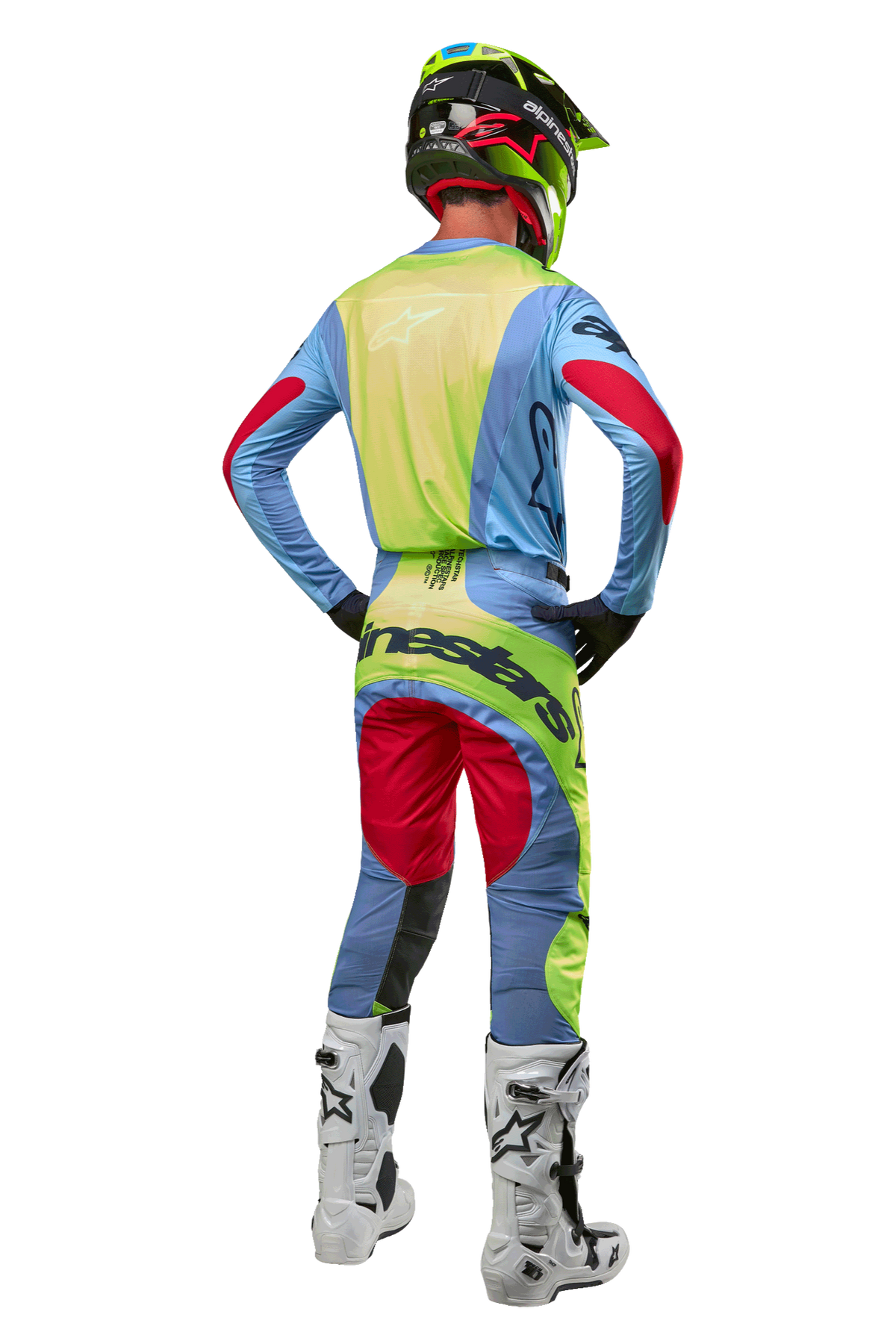 Pilota di motocross visto di spalle con maglia Alpinestars Techstar Ocuri 2024, celeste con accenti giallo fluo e rosso berry, pantaloni da gara coordinati, stivali bianchi e casco neon, equipaggiamento completo da fuoristrada per competizioni professionali