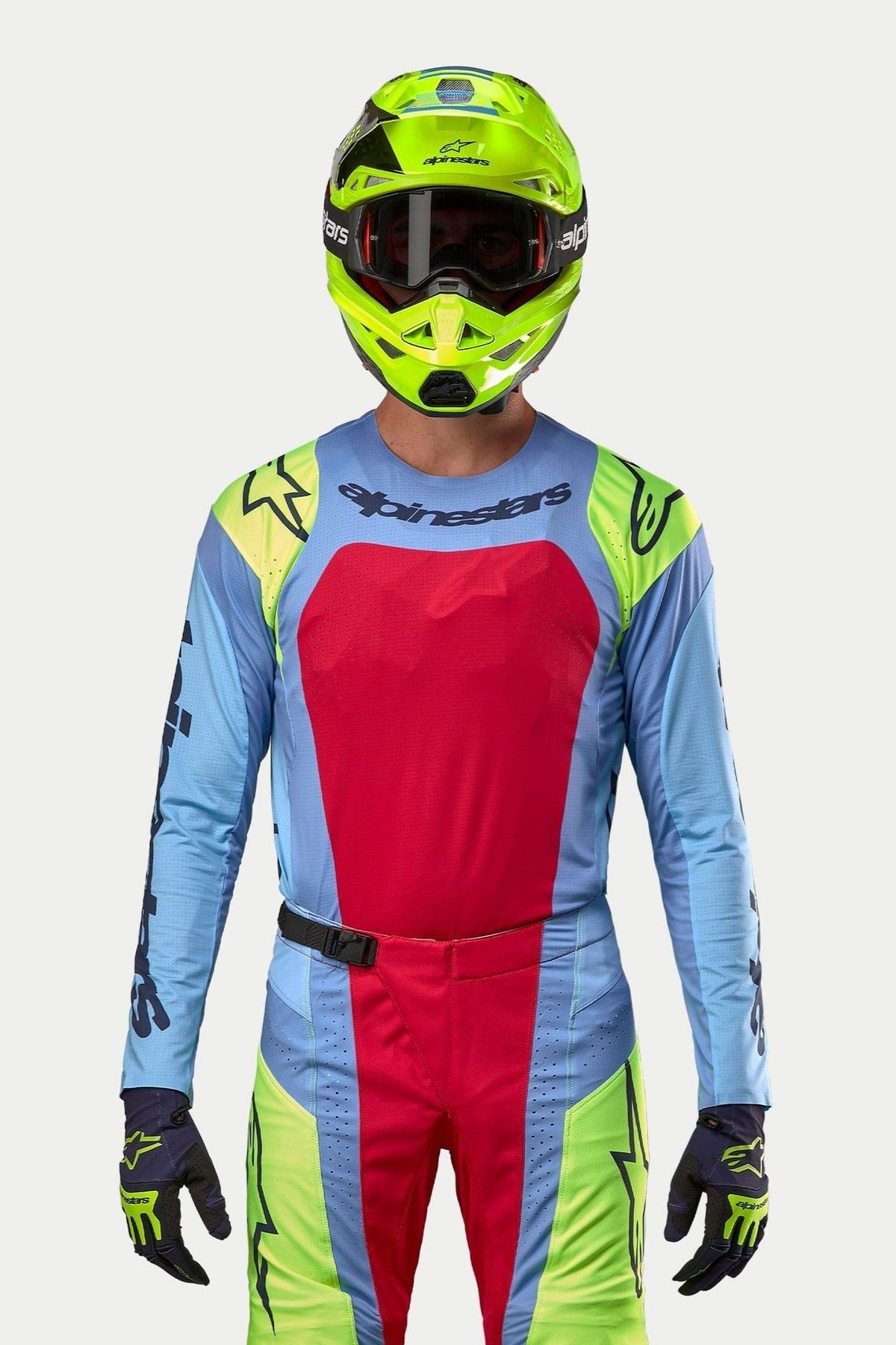 Pilota di motocross con equipaggiamento completo da gara, Maglia Techstar Ocuri 2024 in azzurro con ampio pannello sul petto rosso e accenti sulle spalle giallo fluo, casco giallo fluorescente coordinato, pantaloni coordinati rosso e giallo fluo, abbigliamento professionale per corse fuoristrada