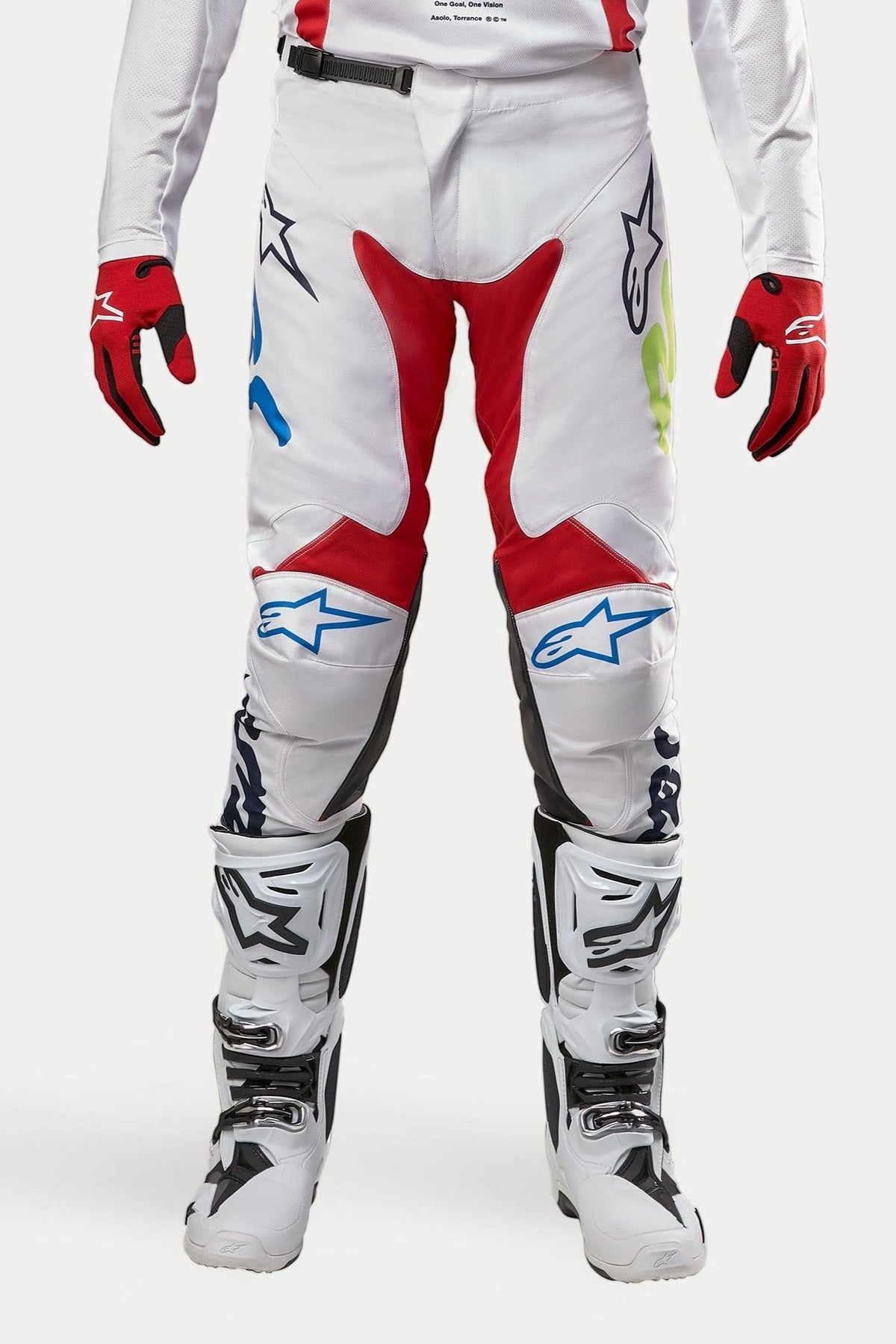 Alpinestars 2024 Racer Hana Pants, pantaloni da motocross, bianco multicolore con accenti rossi, blu e lime, indossati con stivali bianchi e neri e guanti rossi, con loghi Alpinestars sulle ginocchia e design tecnico per il fuoristrada