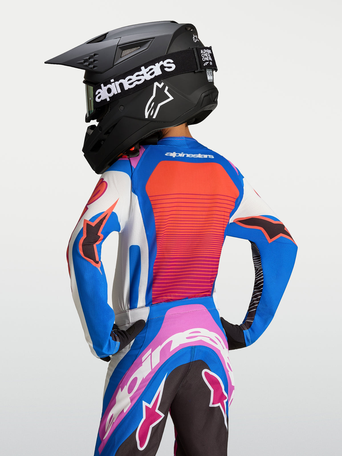 Alpinestars Maglia Supertech Maven Ragazzo, maglia da motocross blu e corallo con mesh traspirante e vestibilità racing, vista posteriore su giovane pilota.