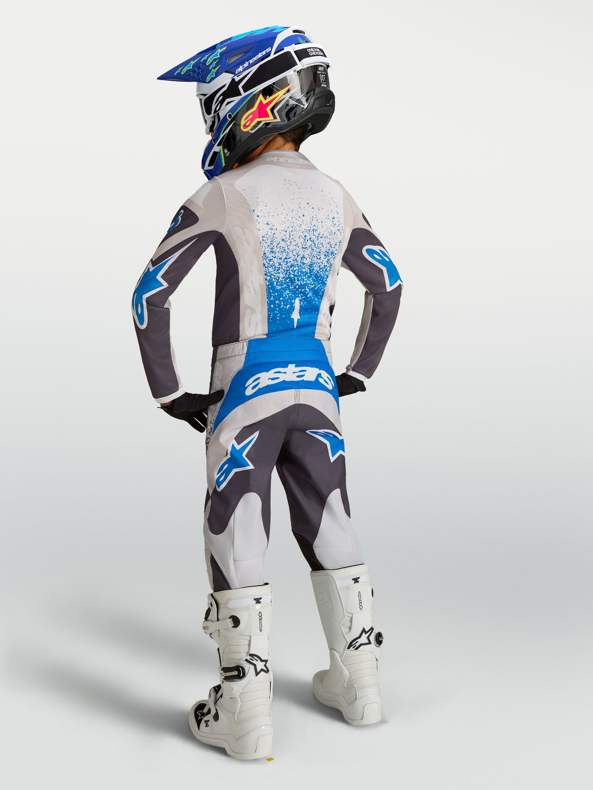 Alpinestars completo motocross Fluid Drag per ragazzo, grigio e blu, vista posteriore su pilota con casco e stivali bianchi.