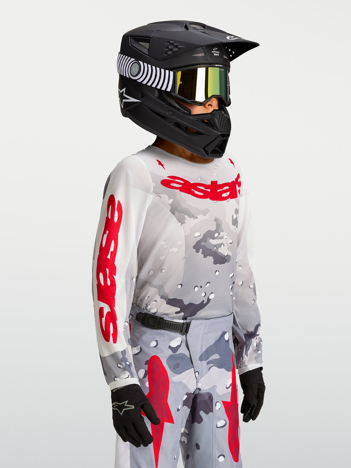 Alpinestars Maglia Fluid Lone Ragazzo 2027, maglia motocross grigia e rossa con motivo camouflage, indossata con casco.