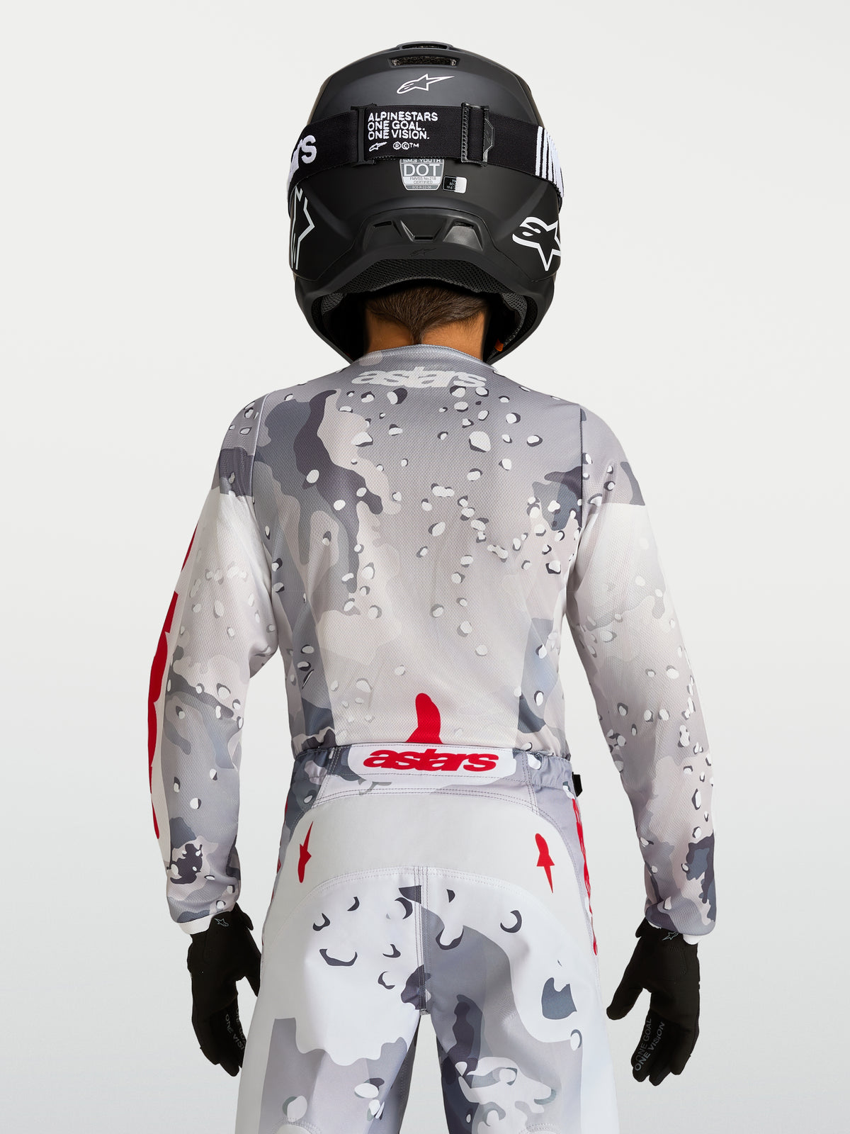 Alpinestars Maglia Fluid Lone Ragazzo 2027, maglia da motocross grigio camouflage, vista posteriore con dettagli rossi e casco nero, abbigliamento off-road per giovani piloti