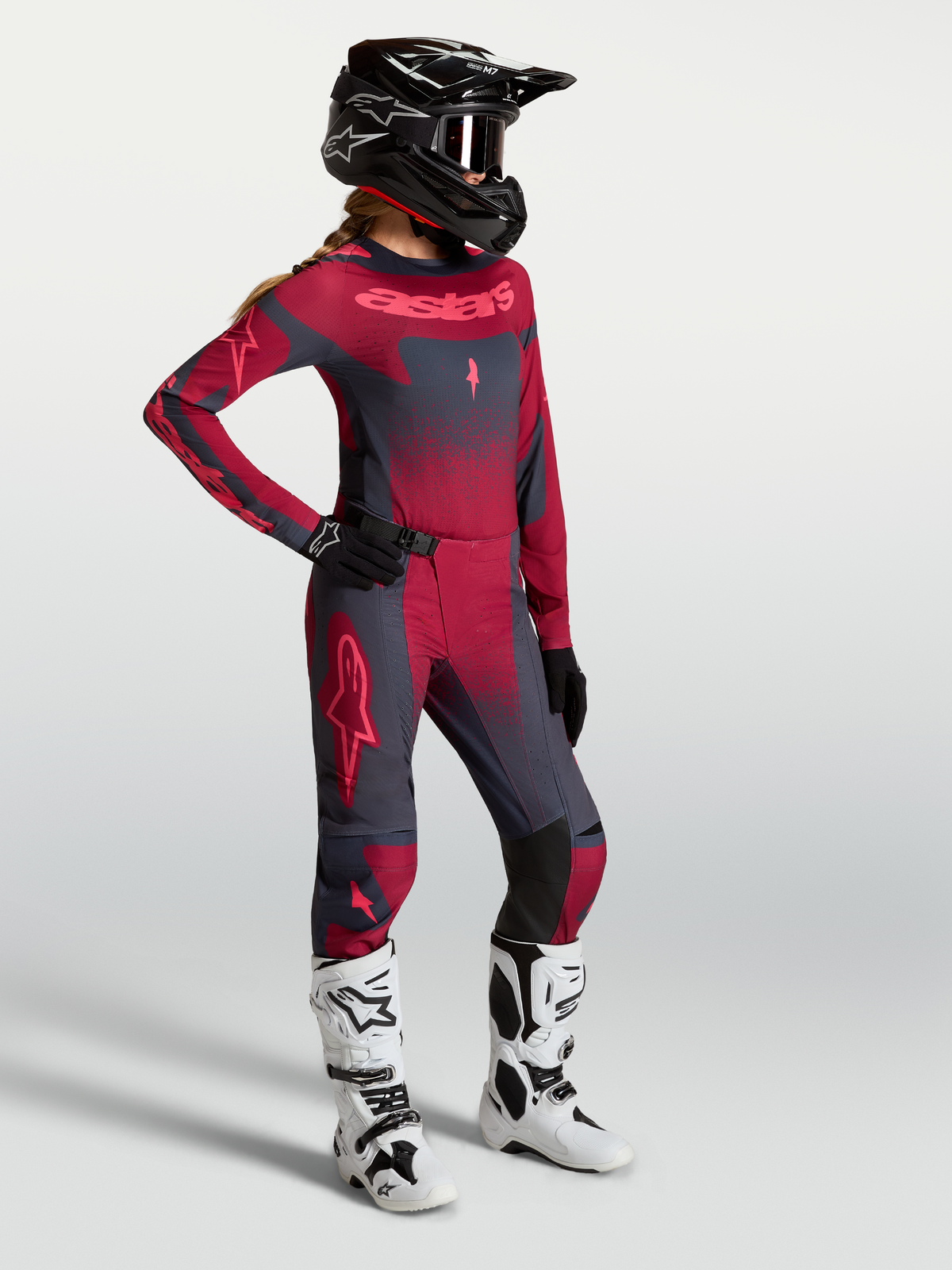 Alpinestars Stella Techstar Swan Gear Set e Pantaloni Stella Techstar Swan, completo da motocross per donna in rosso e grigio scuro, indossato con casco nero e stivali bianchi.