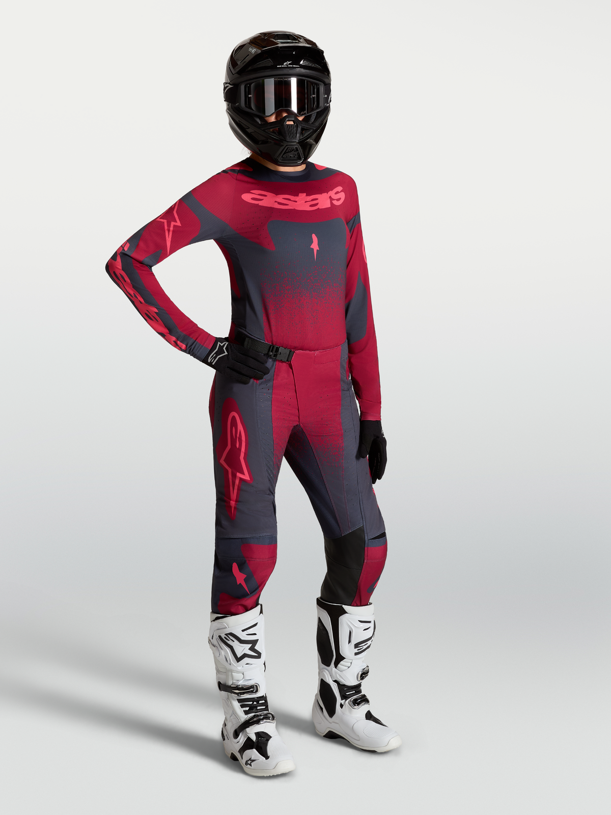 Alpinestars Pantaloni Stella Techstar Swan e maglia, completo motocross da donna grigio scuro e rosso con stivali bianchi.