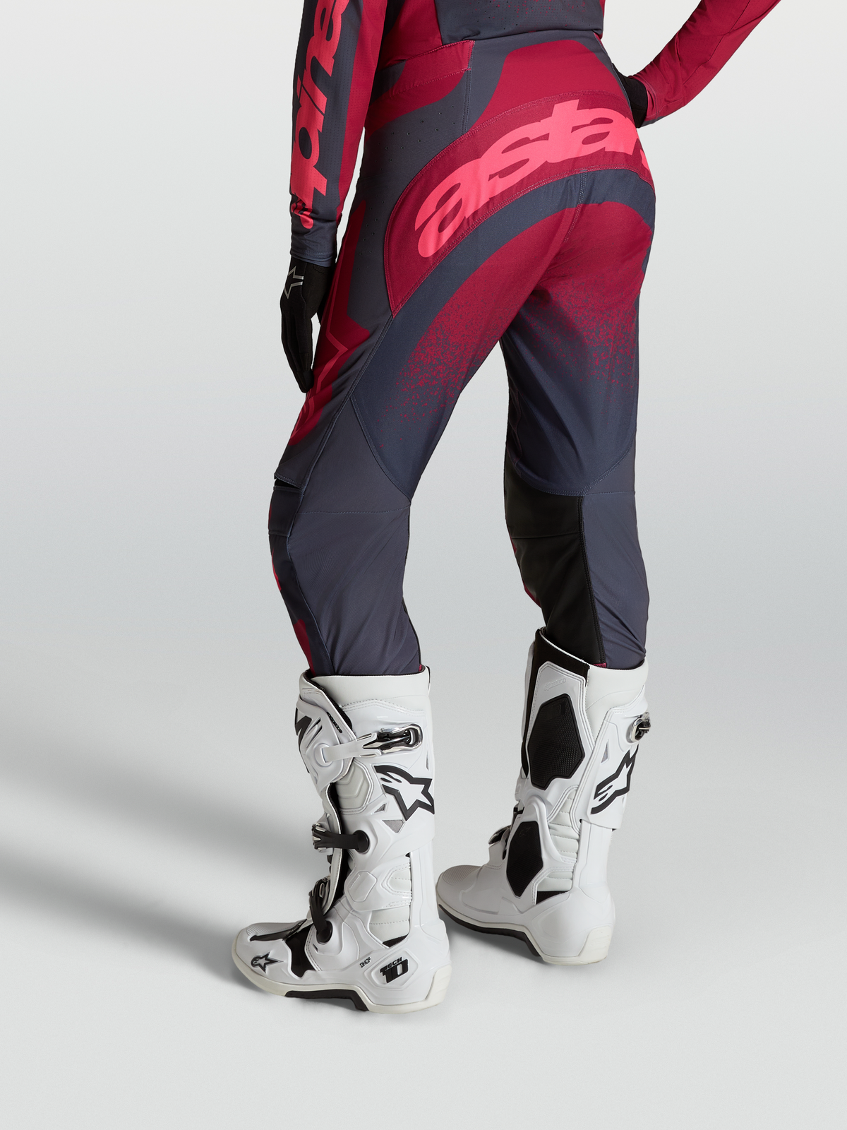 Alpinestars Pantaloni Stella Techstar Swan, pantaloni moto fuoristrada da donna, rosso cremisi e grigio scuro, indossati con stivali Tech 10 bianchi, vista posteriore
